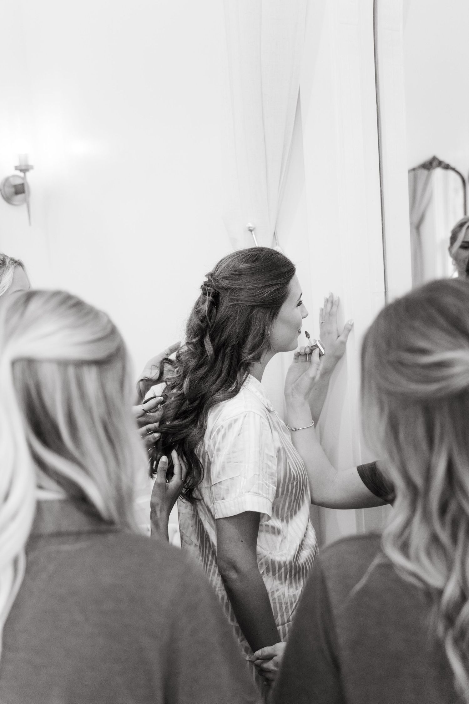 Black and white photo of bride getting makeup applied surrounded by bridesmaids.