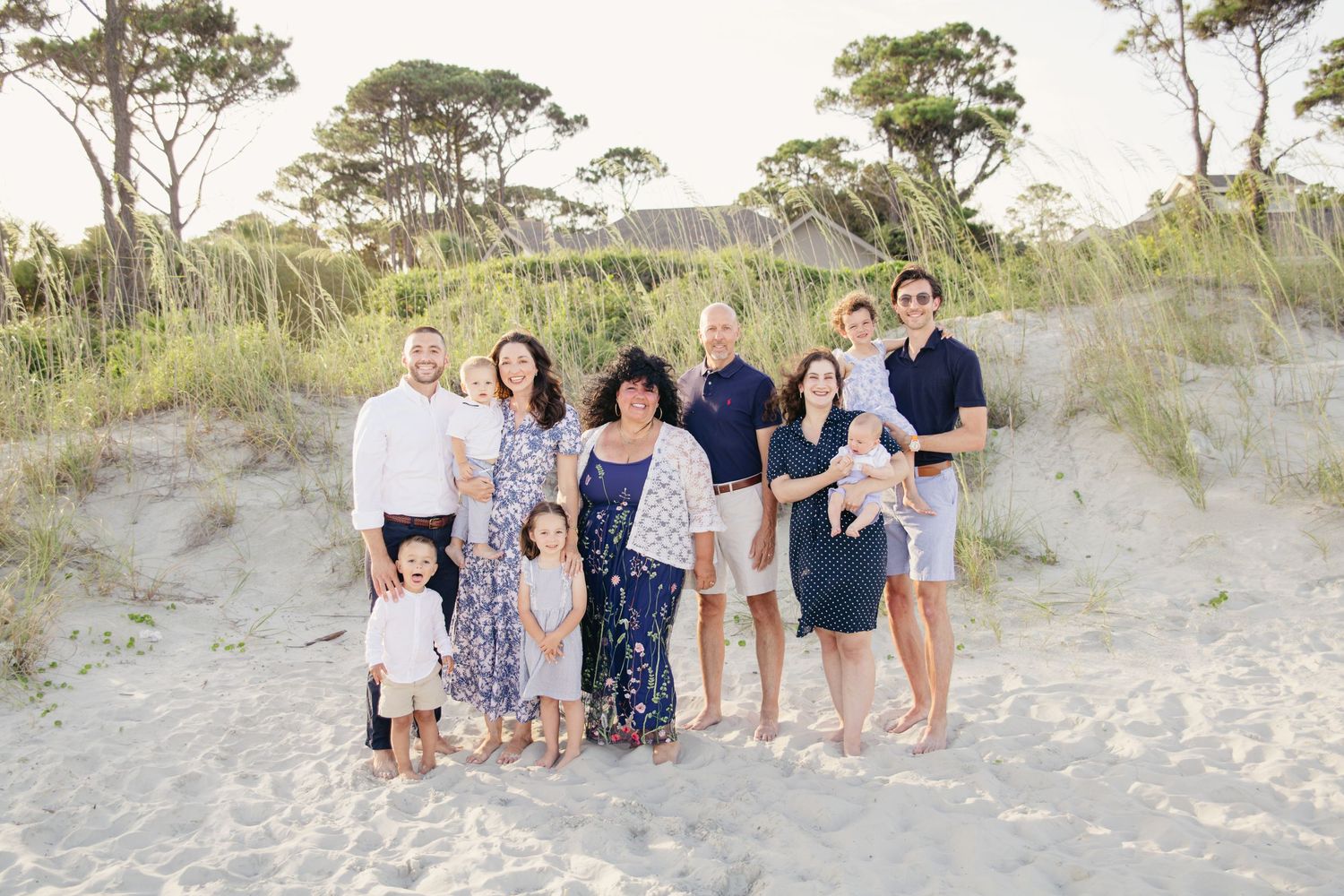 Large extended family group portrait on sandy beach dunes with sea grass and trees.