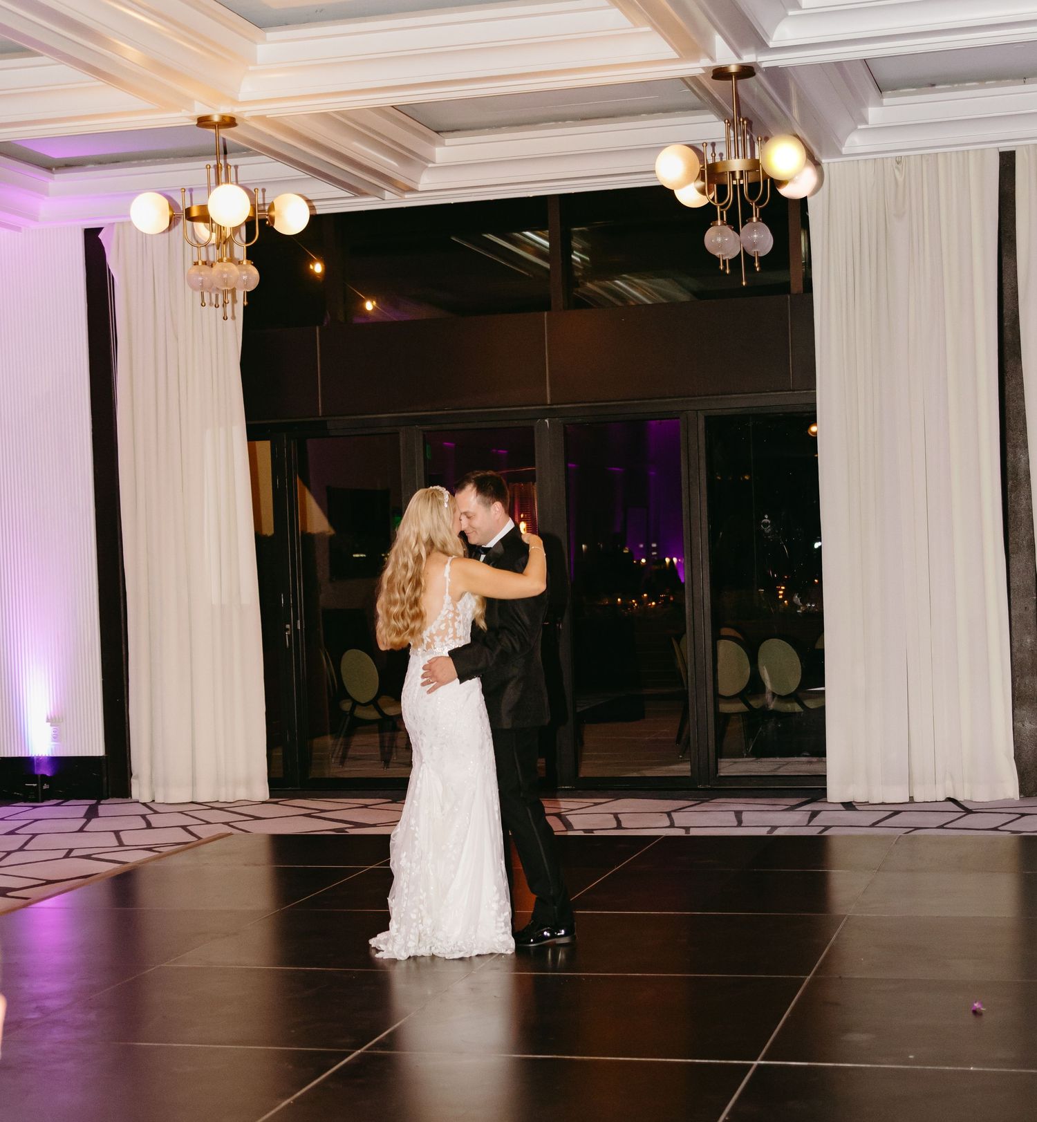 Bride and groom share first dance kiss on black dance floor in elegant ballroom.