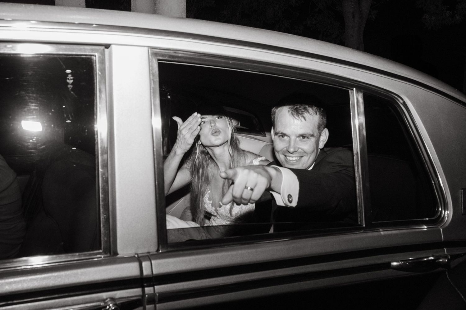 Black and white photo of a couple celebrating in a limousine, flashing rings and smiling.