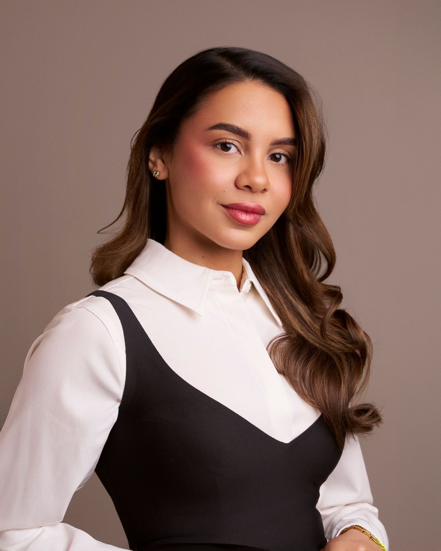 Young woman in black and white outfit poses professionally against brown background.