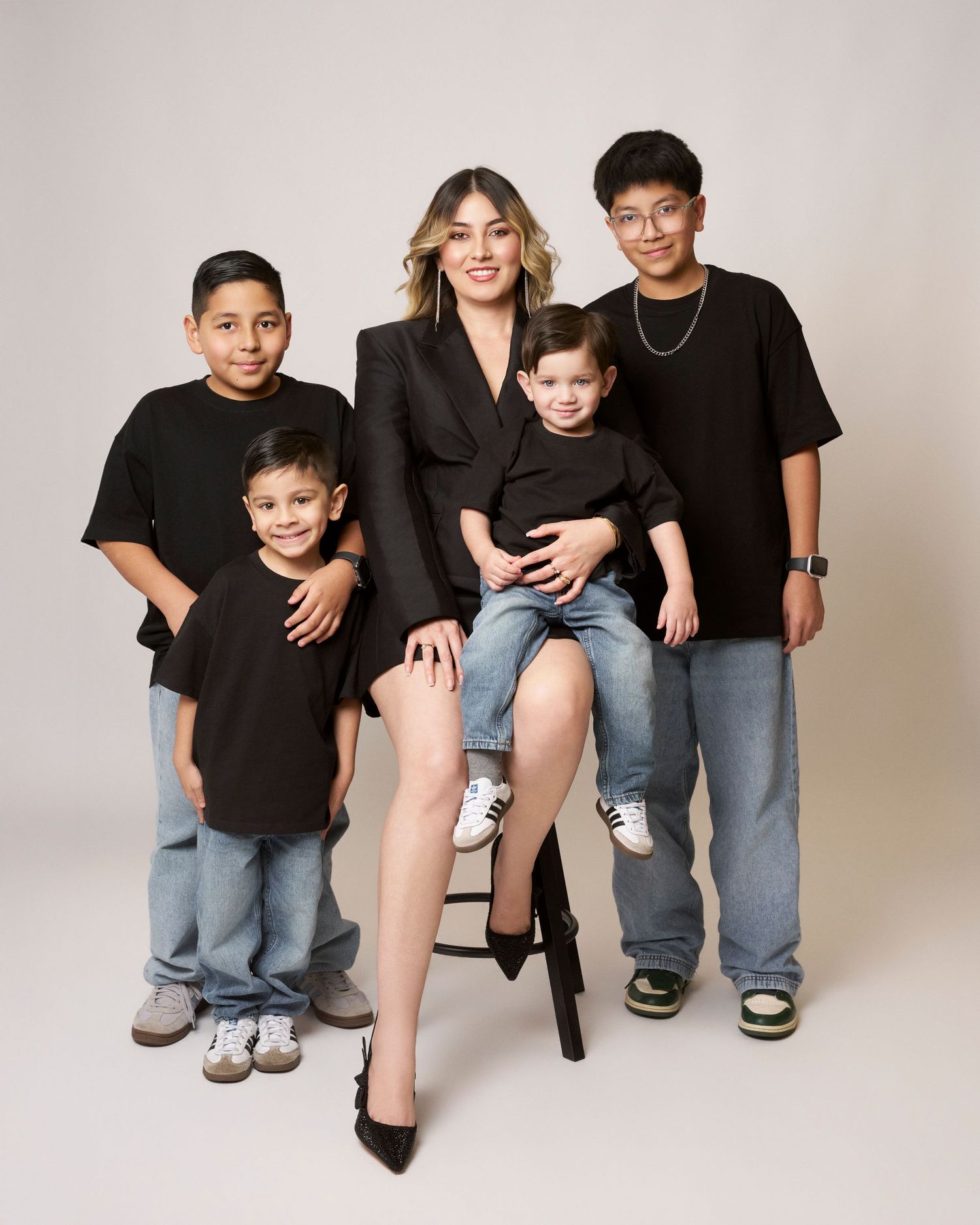 Woman in black blazer poses with four boys in matching black outfits for family portrait.