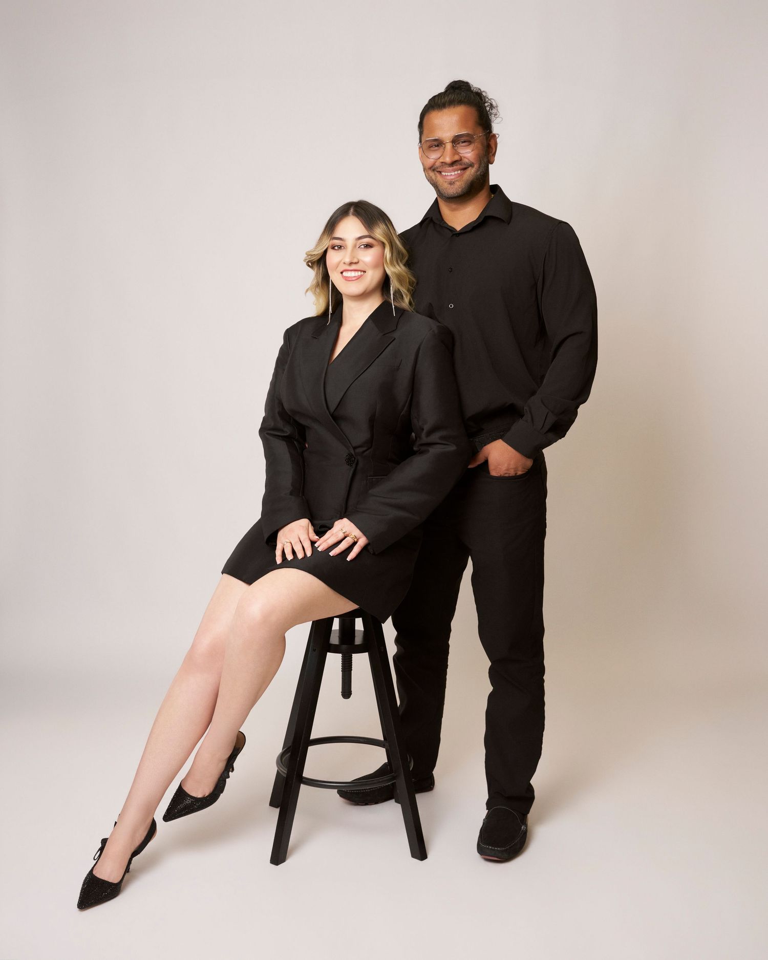 Couple in coordinating black outfits pose together for elegant studio portrait.