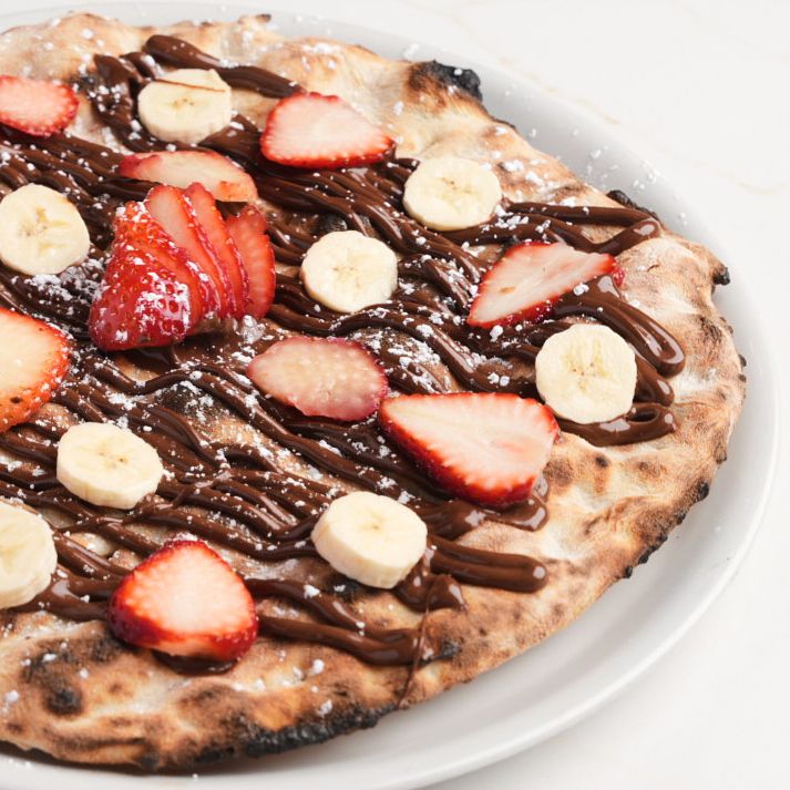 Dessert pizza topped with Nutella, fresh strawberries, banana slices, and powdered sugar.