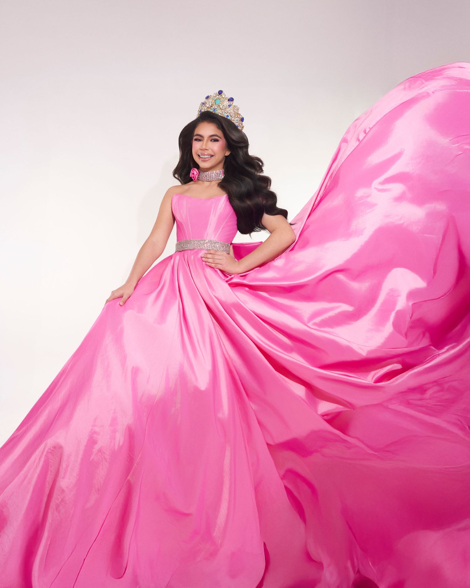Woman in flowing pink ball gown with crown posing dramatically.