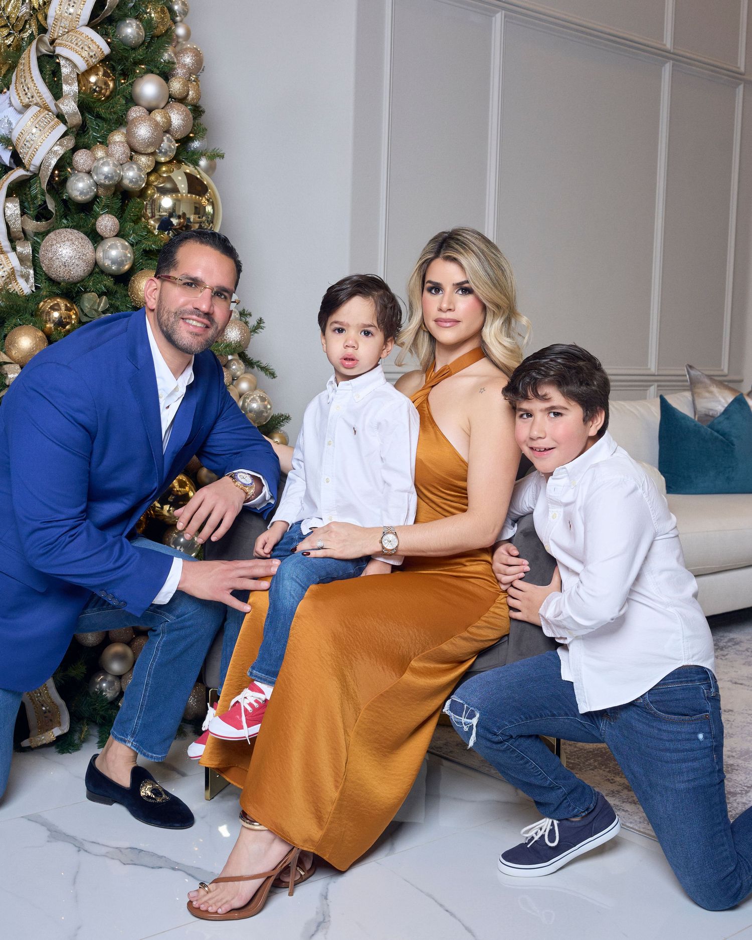 Family of four poses by decorated Christmas tree in festive holiday portrait.