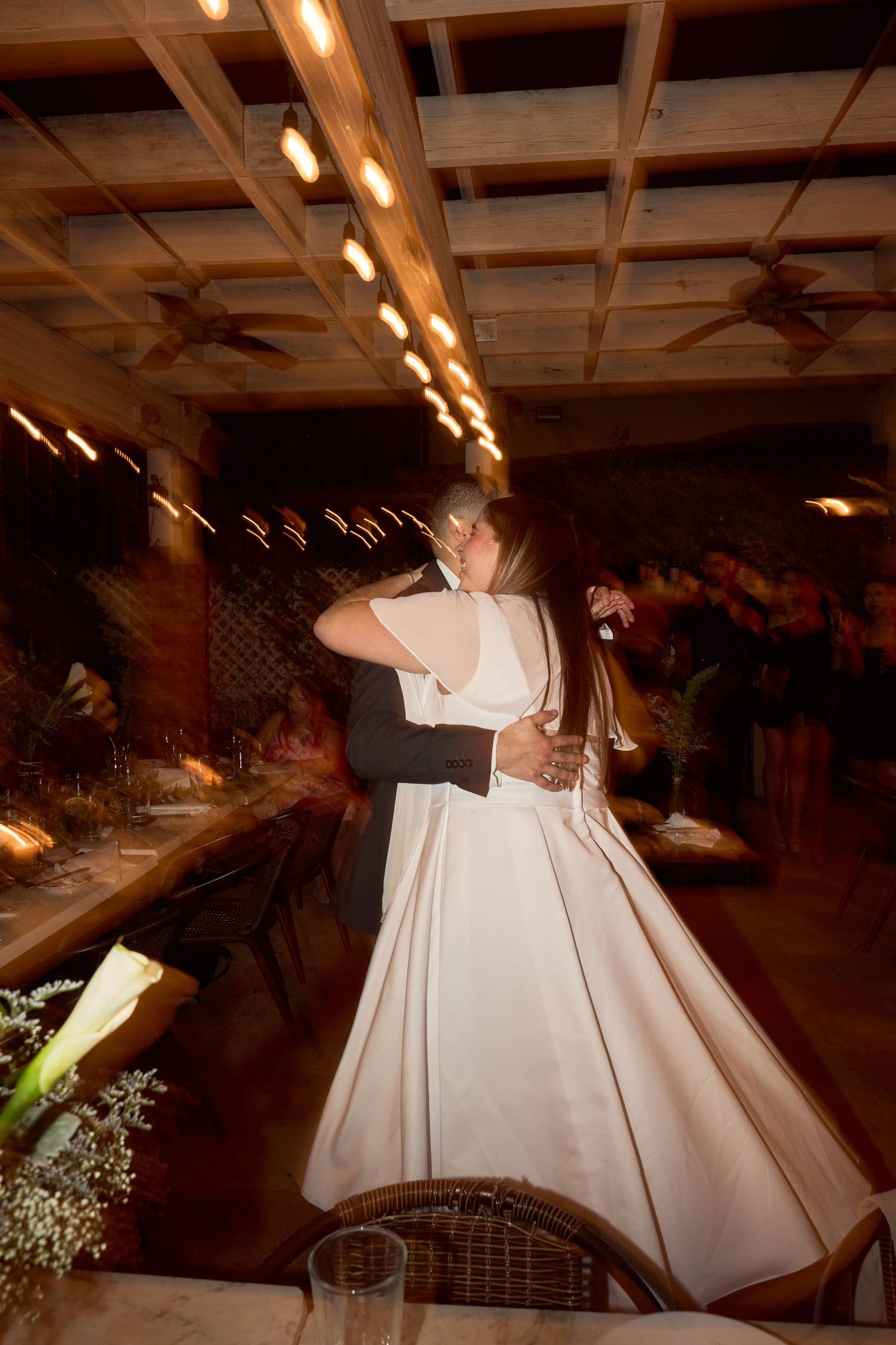 Bride and groom share their first dance in a warmly lit reception venue with a motion blur effect.