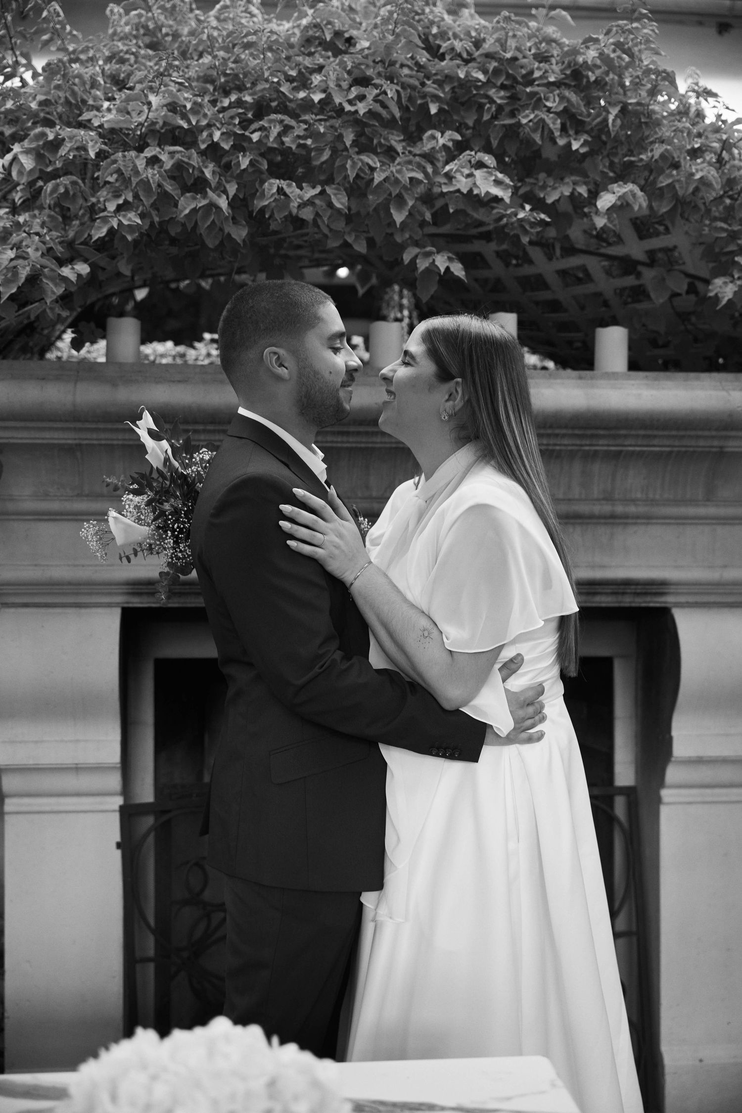 Bride and groom sharing first kiss in black and white wedding photo outdoors near fireplace.