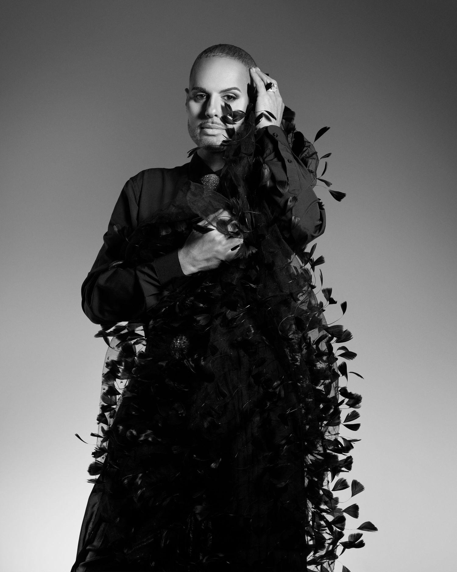 Black and white portrait of woman in feathered black gown against gray background.