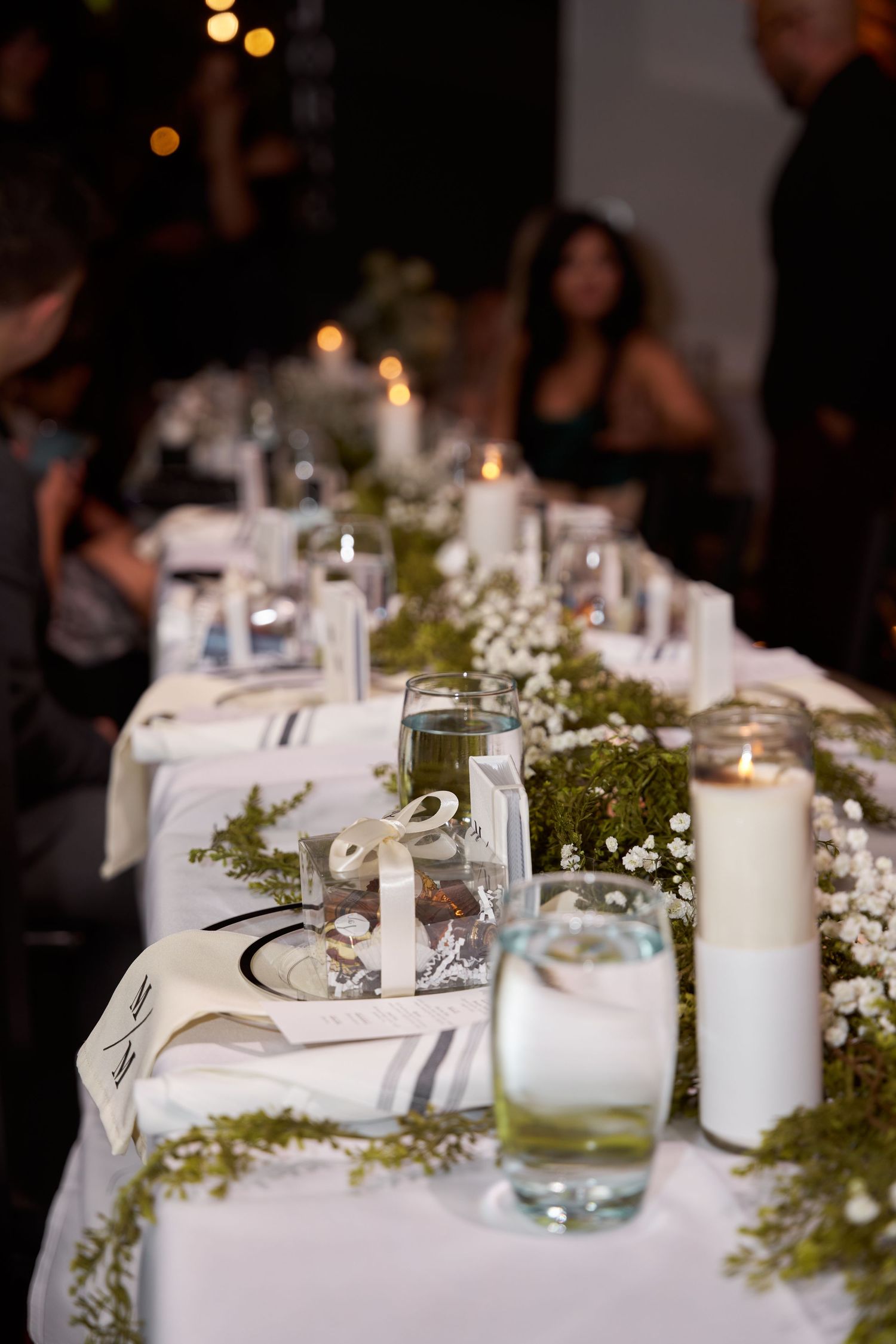 Elegant wedding reception table decorated with white candles, greenery, and delicate floral arrangements.