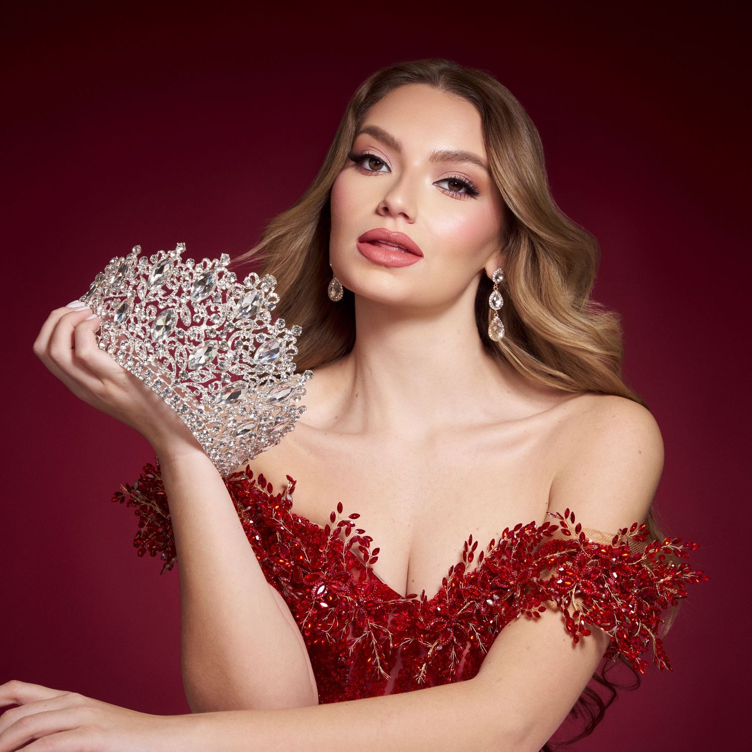 Elegant woman in red off-shoulder gown holds a crystal heart-shaped clutch with matching drop earrings.