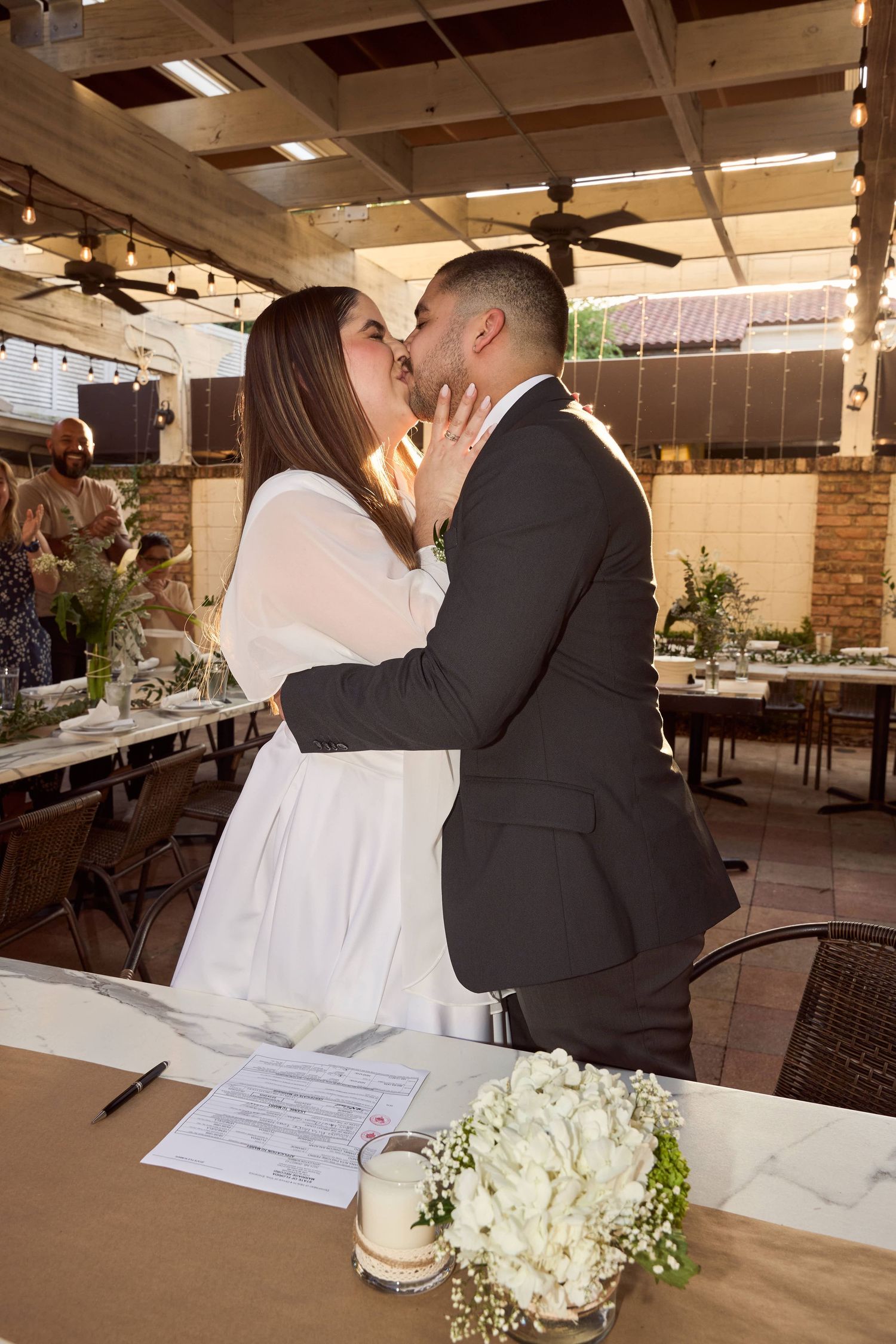 Bride and groom share first kiss after signing marriage certificate at rustic outdoor wedding venue.