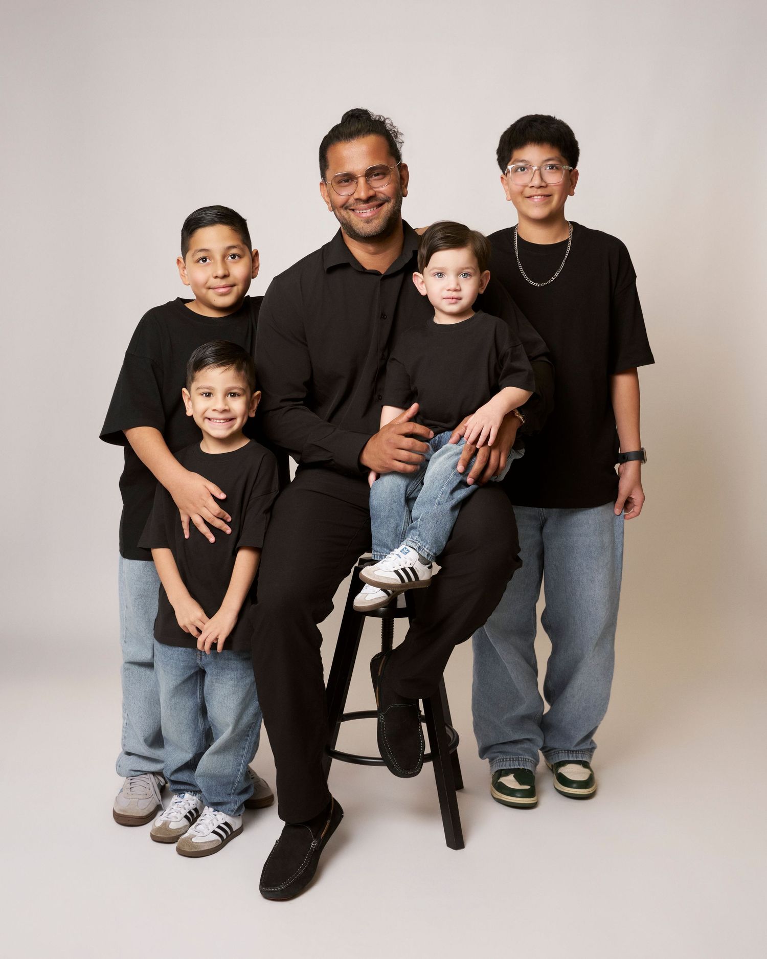 Man in black shirt poses with four boys in matching black outfits for family portrait.