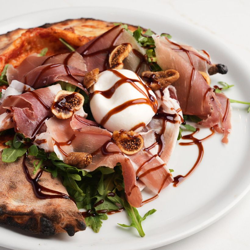 Neapolitan pizza topped with prosciutto, burrata, arugula, dried figs, and balsamic drizzle.