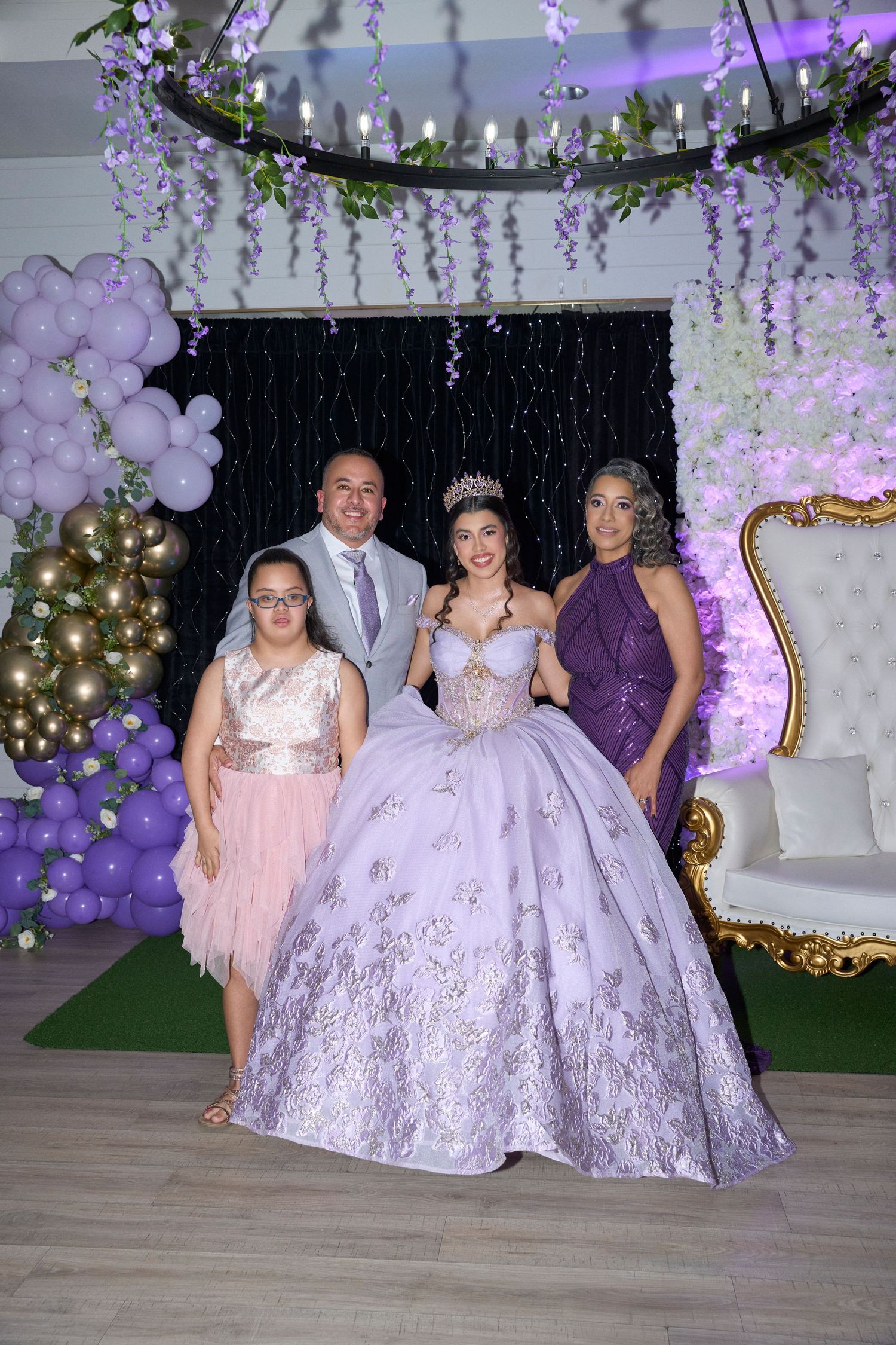 A young woman in a lavender quinceañera gown and tiara poses with three guests at an elegant purple-themed celebration.