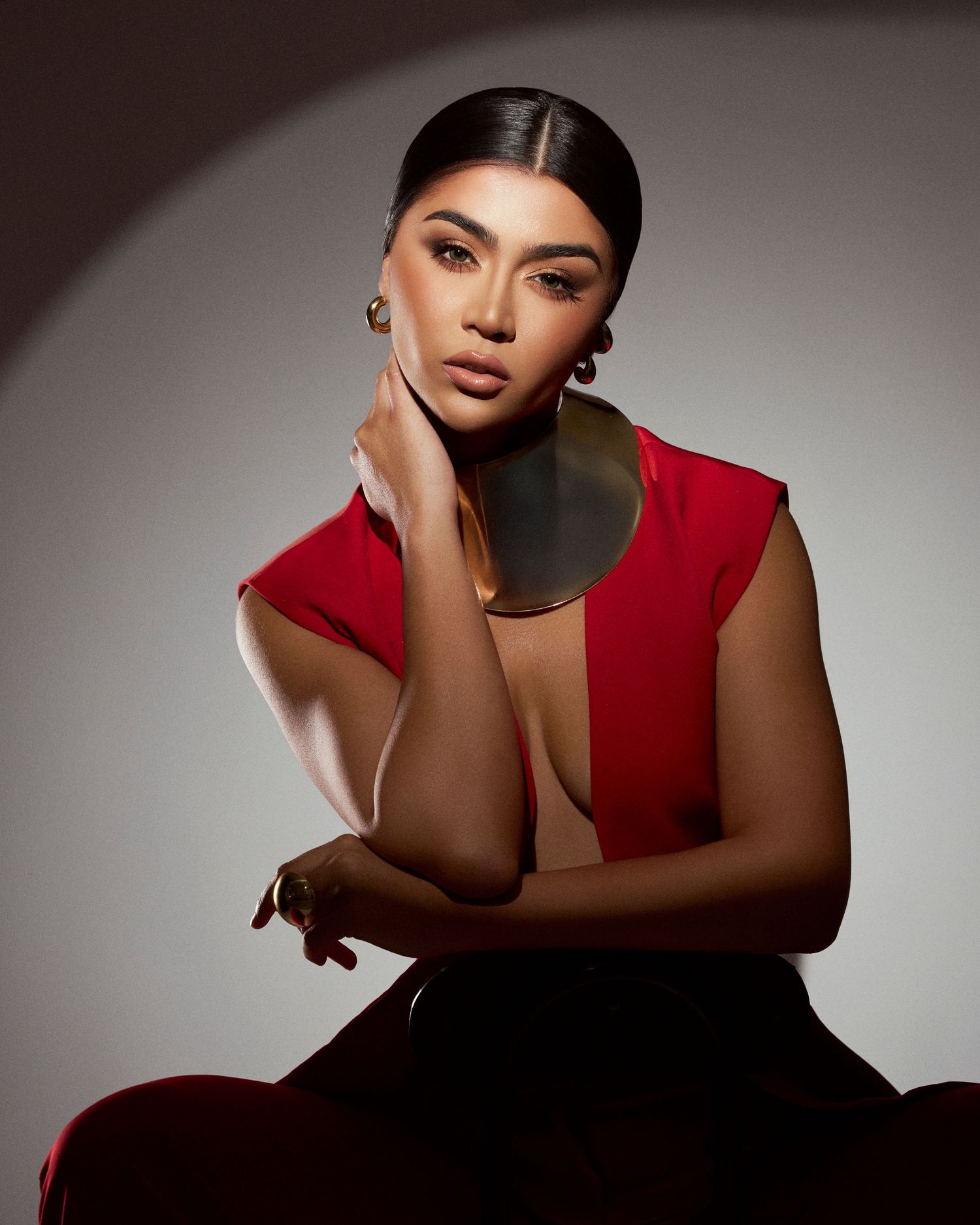 Woman in red sleeveless top poses confidently with hand on cheek in a professional studio portrait.