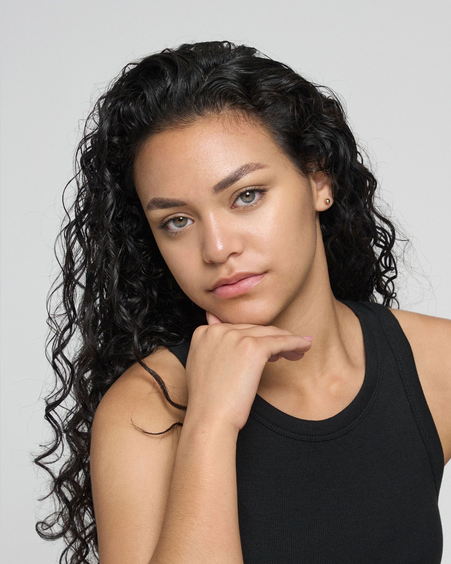 Close-up portrait of woman with long curly black hair wearing black tank top.