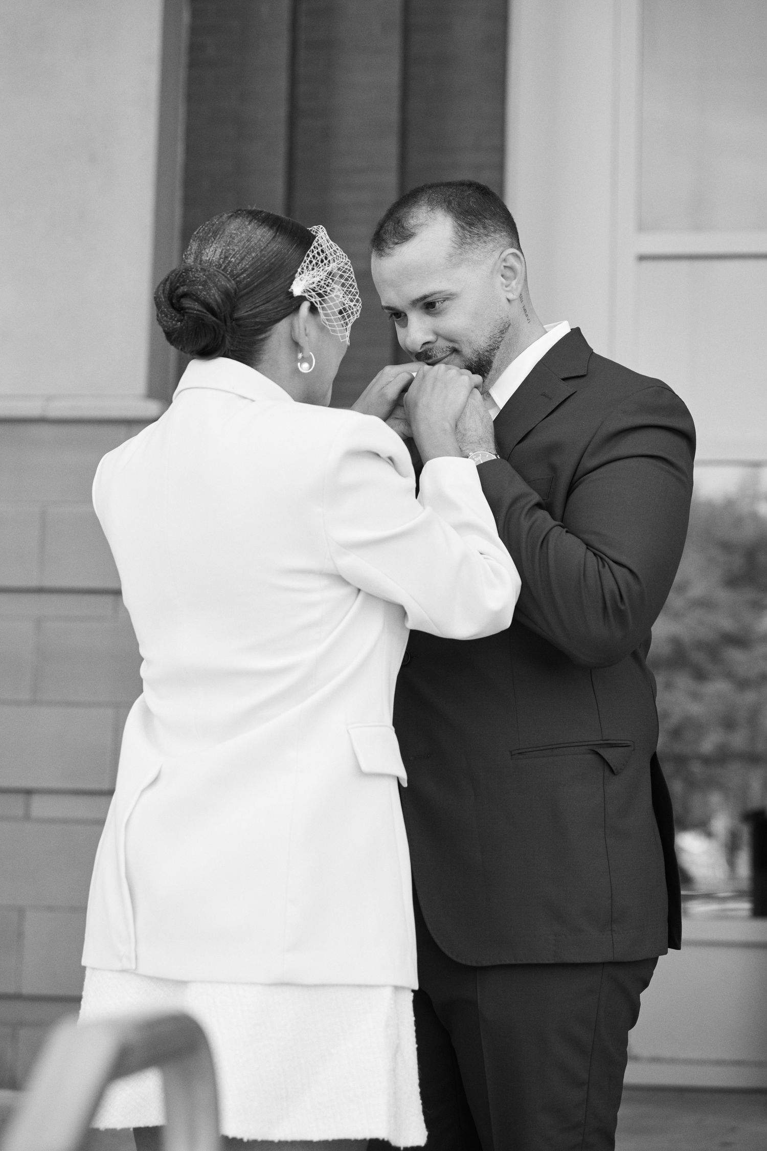 Bride and groom share tender moment as he kisses her hands during black and white wedding portrait.