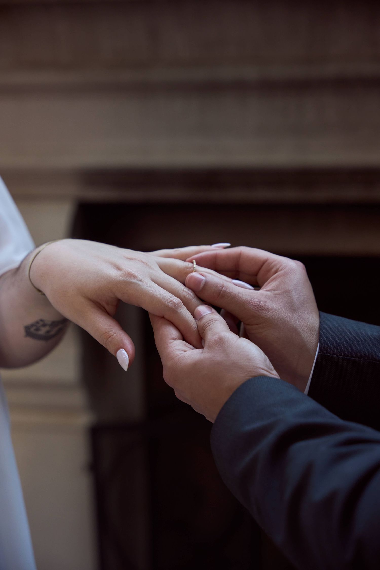 Groom placing a wedding ring on brides finger during ceremony, with tattoo visible on brides wrist.