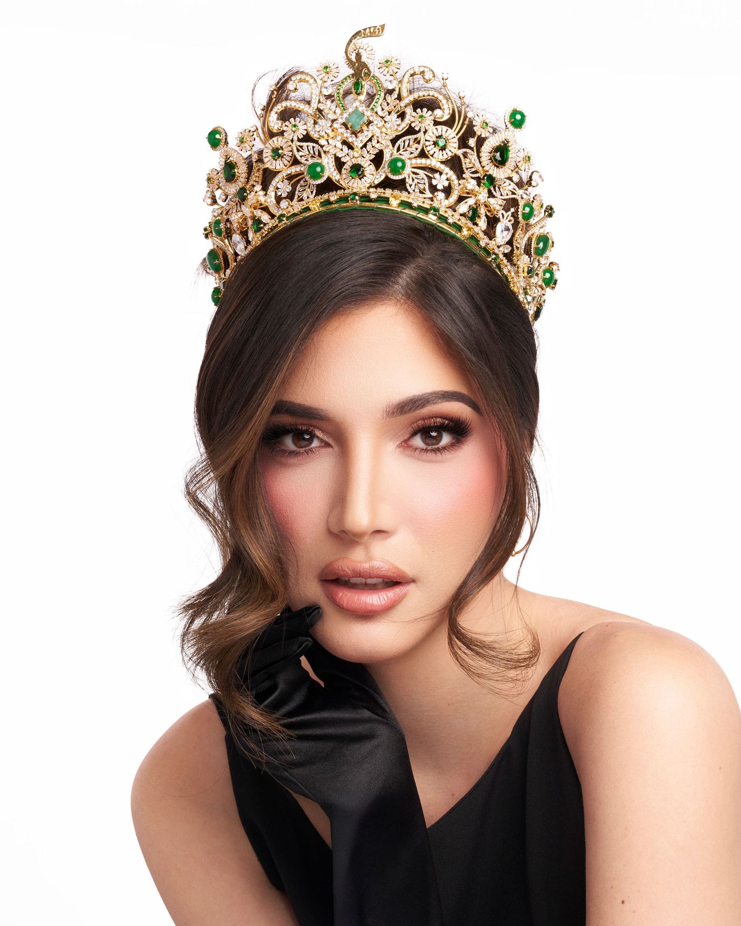 Woman wearing gold crown with emerald gems in black satin gloves.
