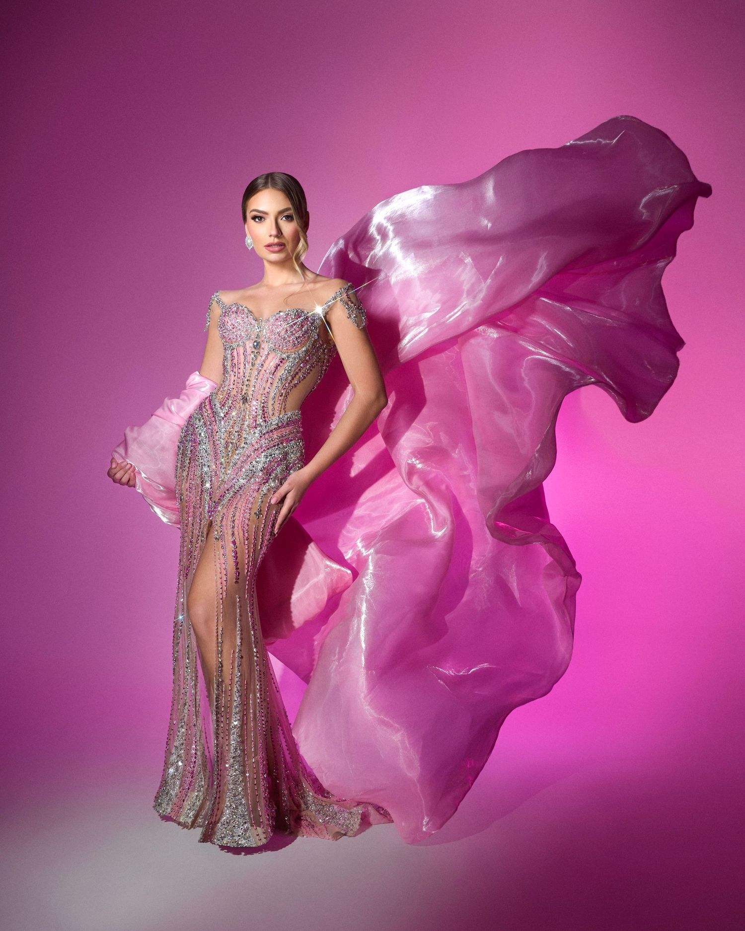 Model in pink flowing gown with billowing fabric poses against vibrant pink background.