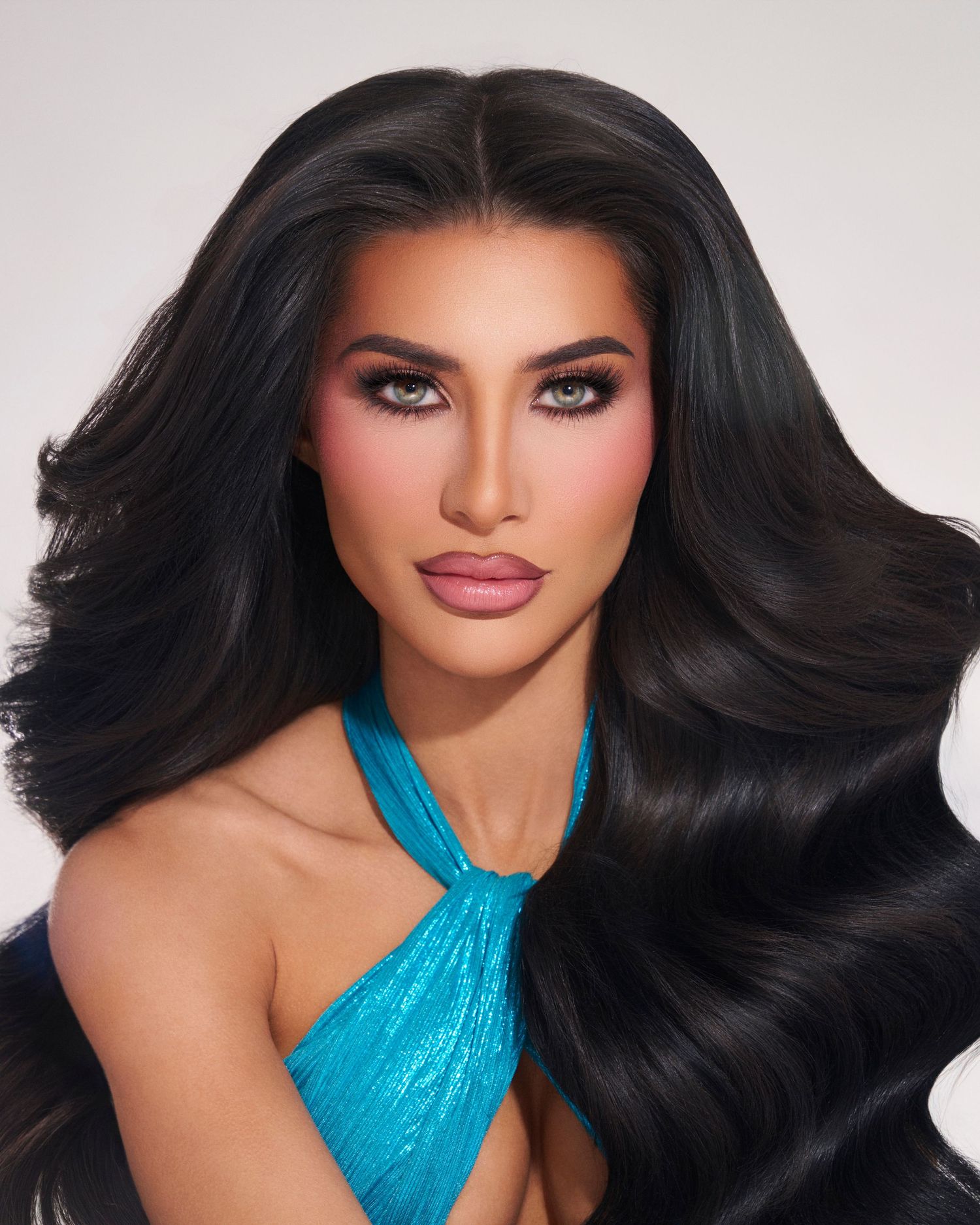 Woman with long black wavy hair wearing turquoise halter top poses for glamour beauty portrait.