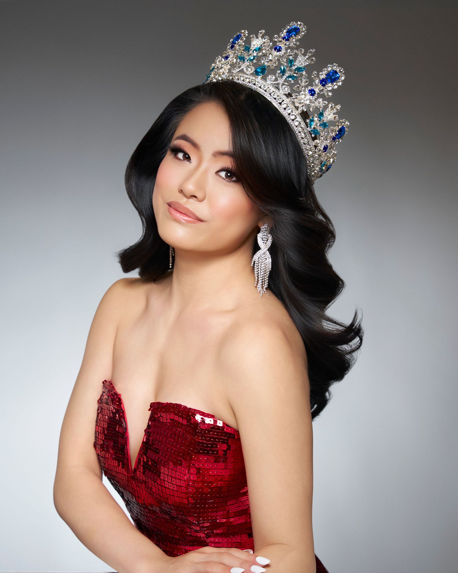 Woman in red sequin dress wearing blue and silver pageant crown.