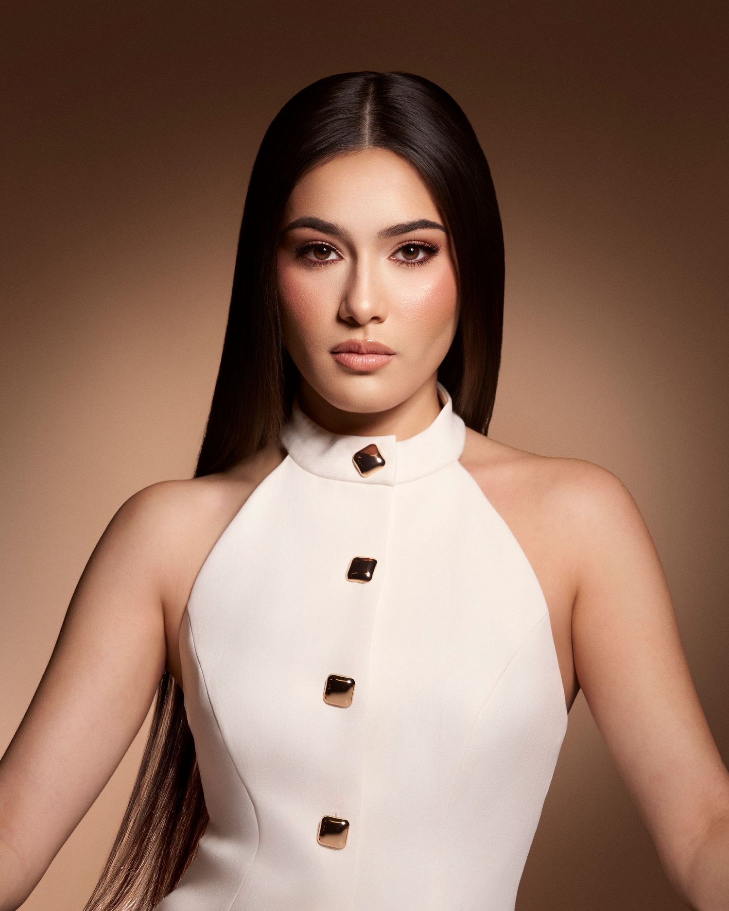 Woman with long straight black hair wearing a white sleeveless halter top with gold buttons.