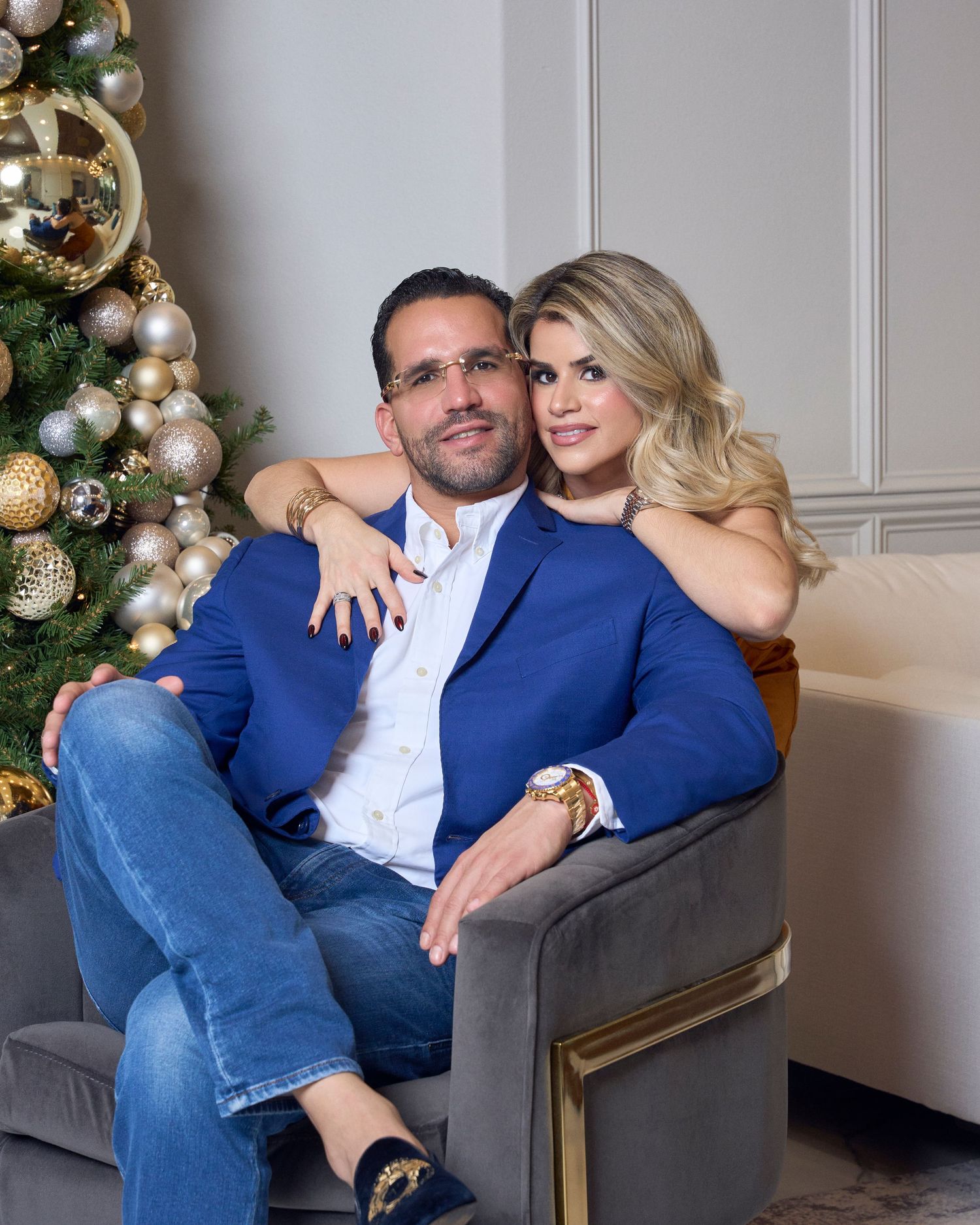 Couple embraces in armchair beside decorated Christmas tree in cozy holiday portrait.