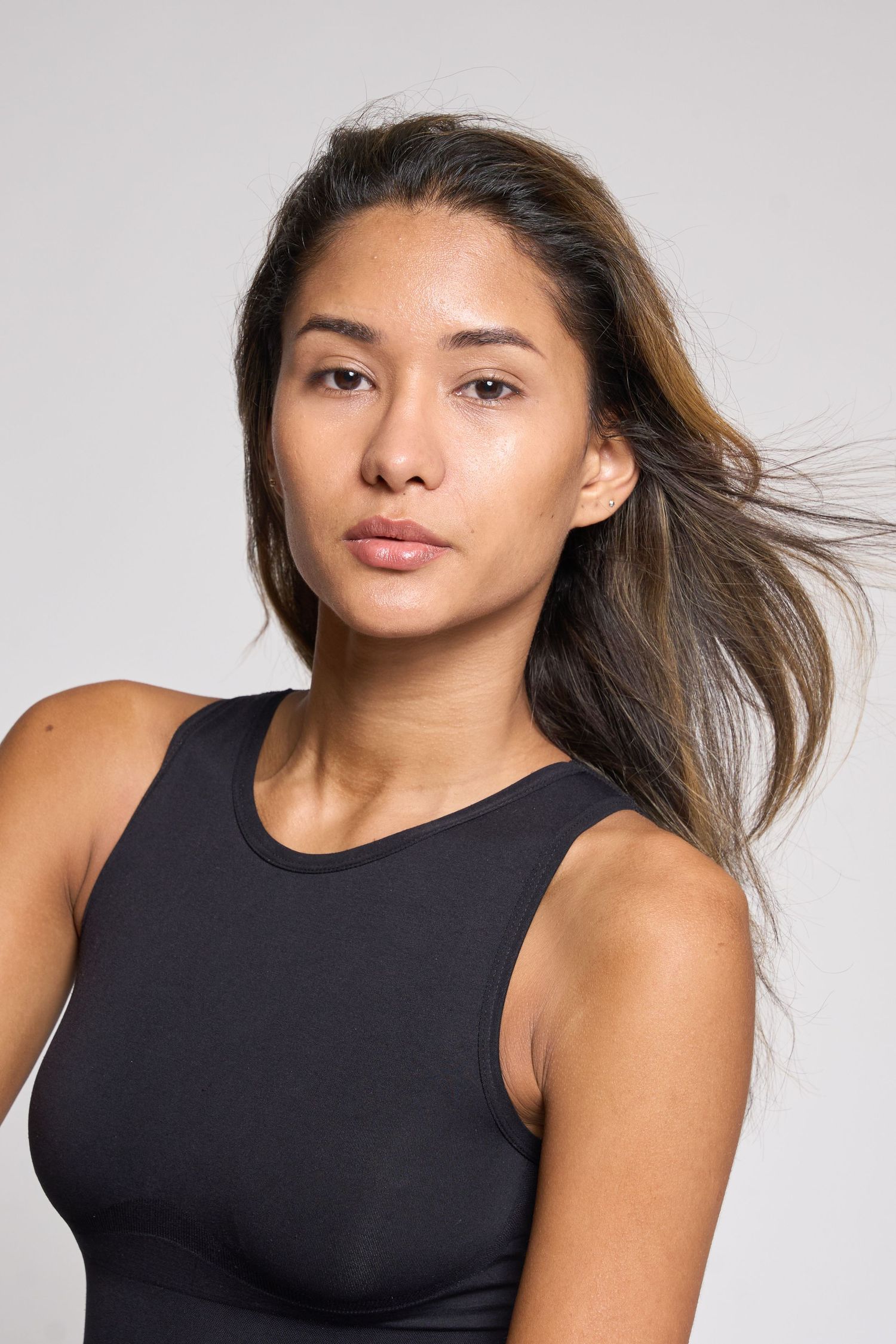 Natural beauty portrait of a woman in a black tank top with flowing dark hair on a gray background.