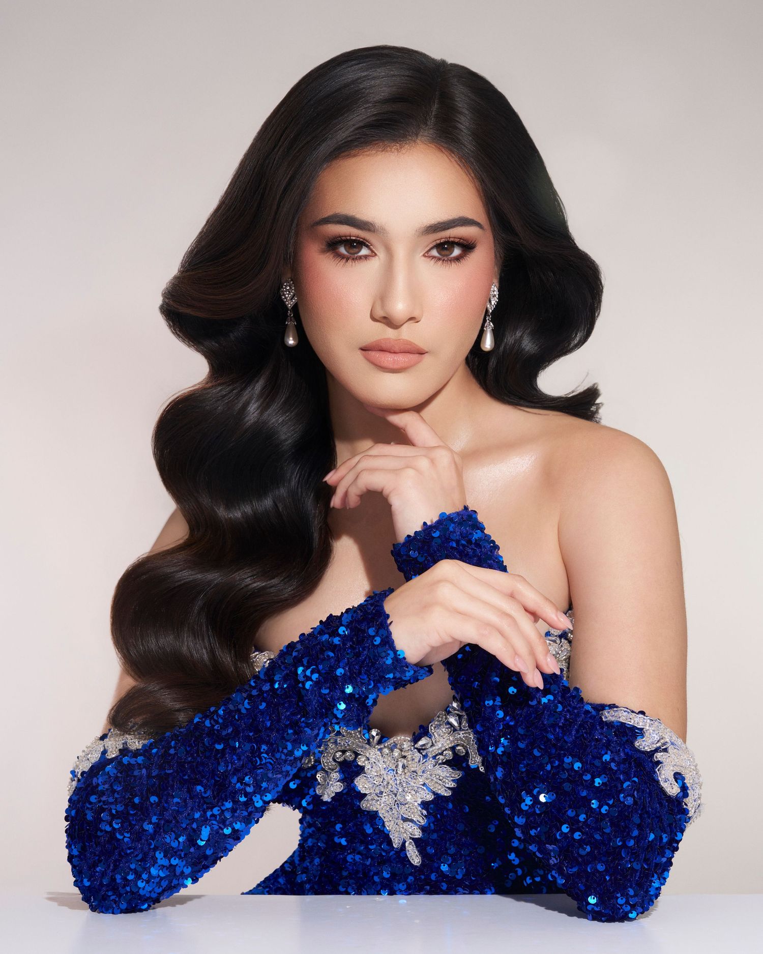 Woman in blue sequin gown with silver accessories posing elegantly.