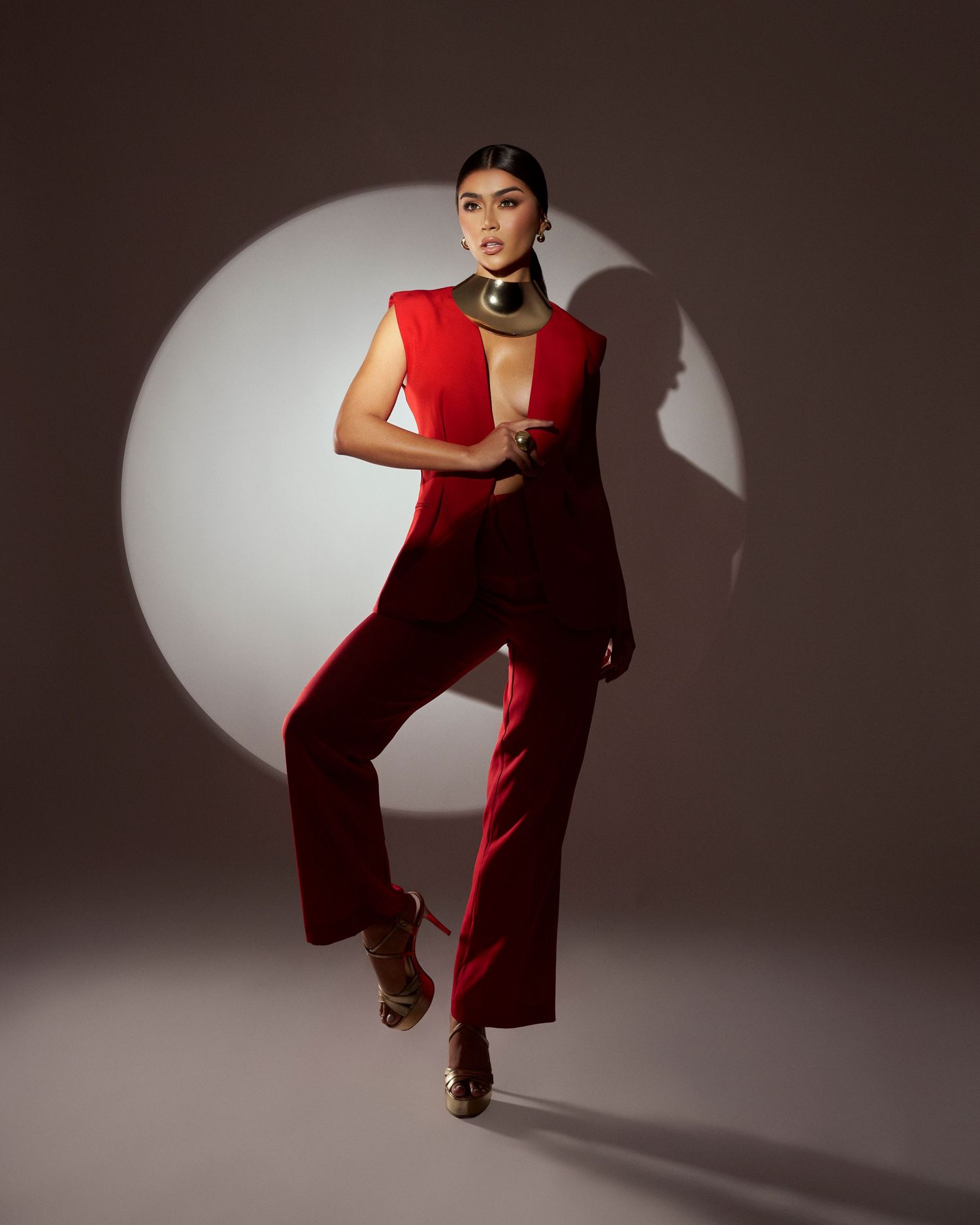 Woman in red jumpsuit with gold collar poses in spotlight on gray background.