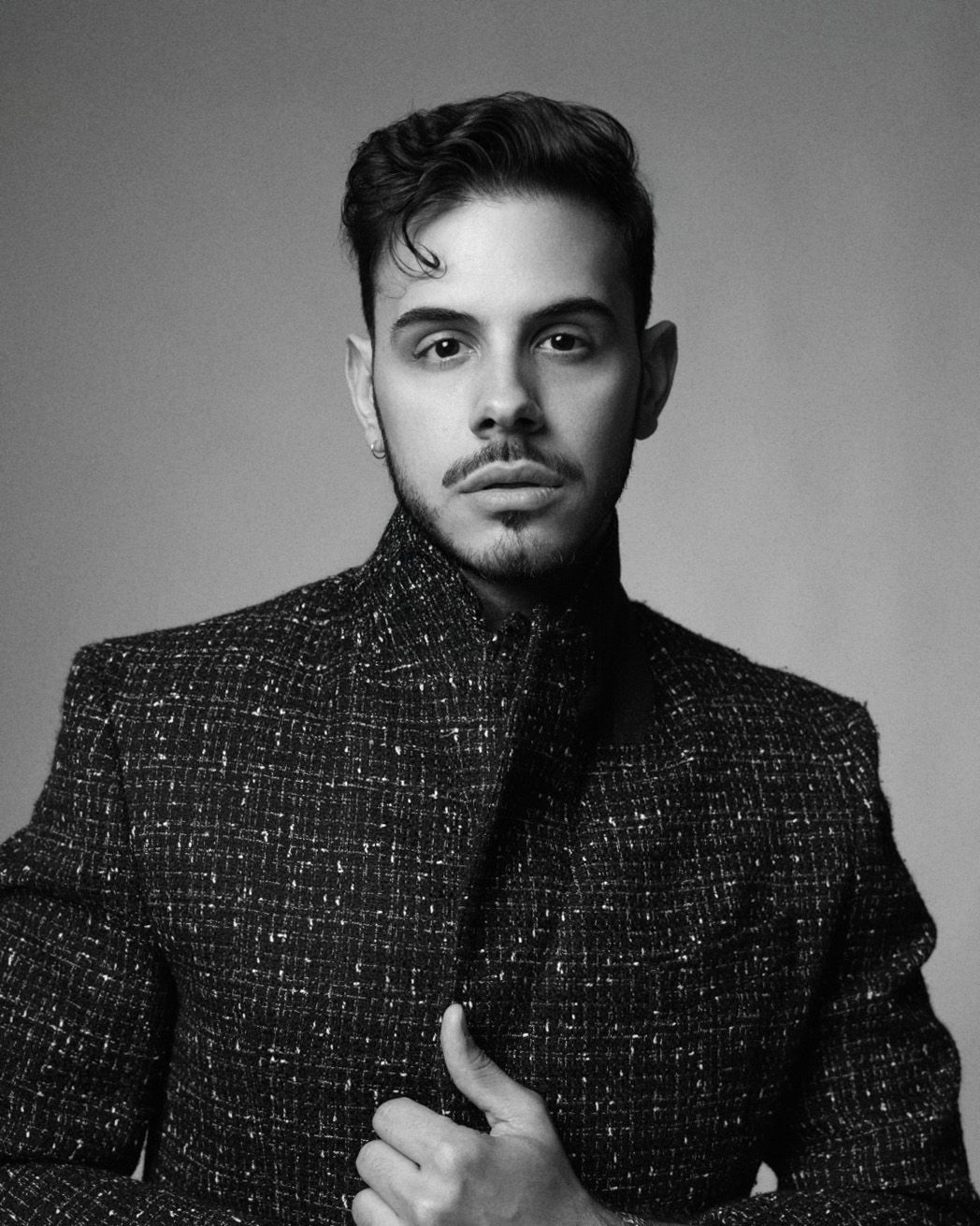 Stylish man in textured tweed jacket poses in dramatic black and white studio fashion portrait.