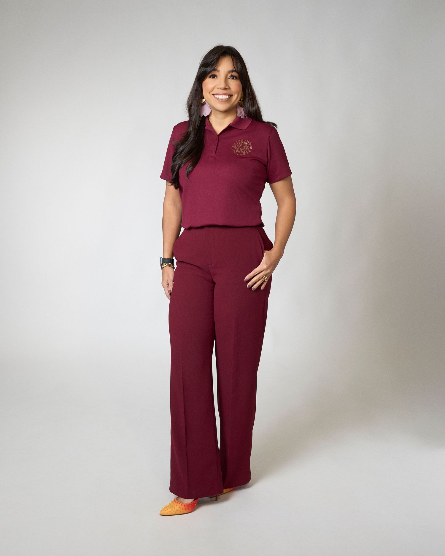 Woman smiling in burgundy polo shirt and wide-leg pants with orange heels.