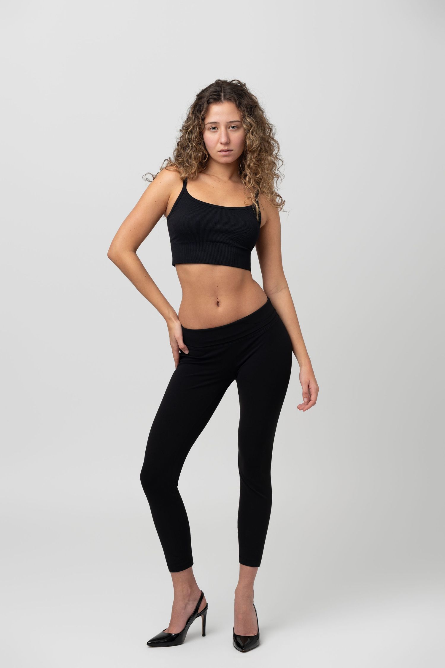 Full-body studio portrait of a female model in black outfit on a clean white background, showcasing a natural pose for modelling digitals.