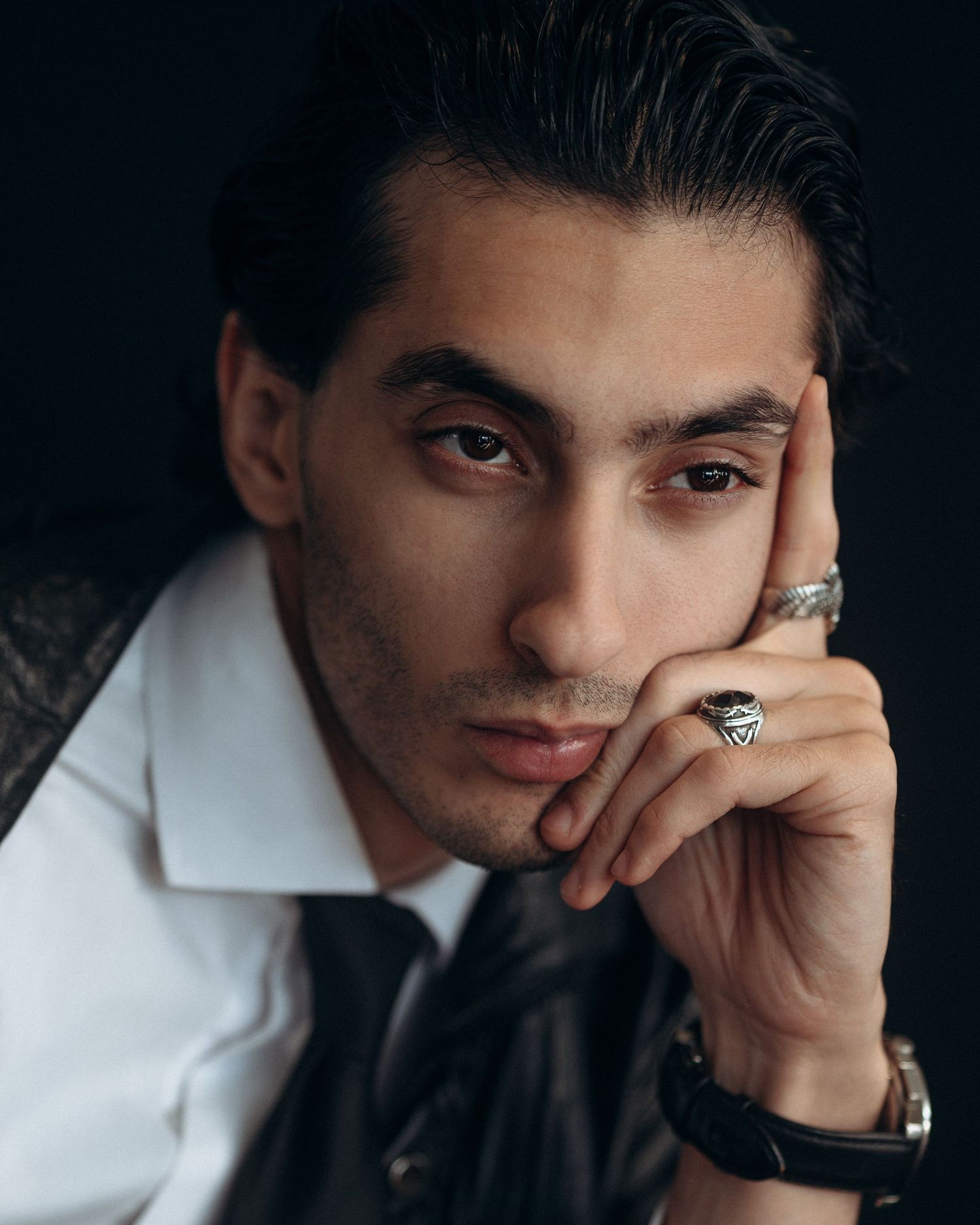 Moody male portrait with hand-to-face pose, styled in formalwear and captured with soft directional lighting.