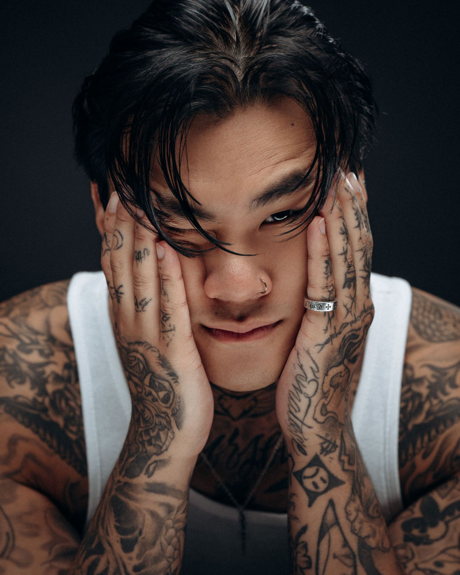 Expressive portrait of a tattooed male model with hands on face, photographed in a dark studio setting by Montreal photographer.