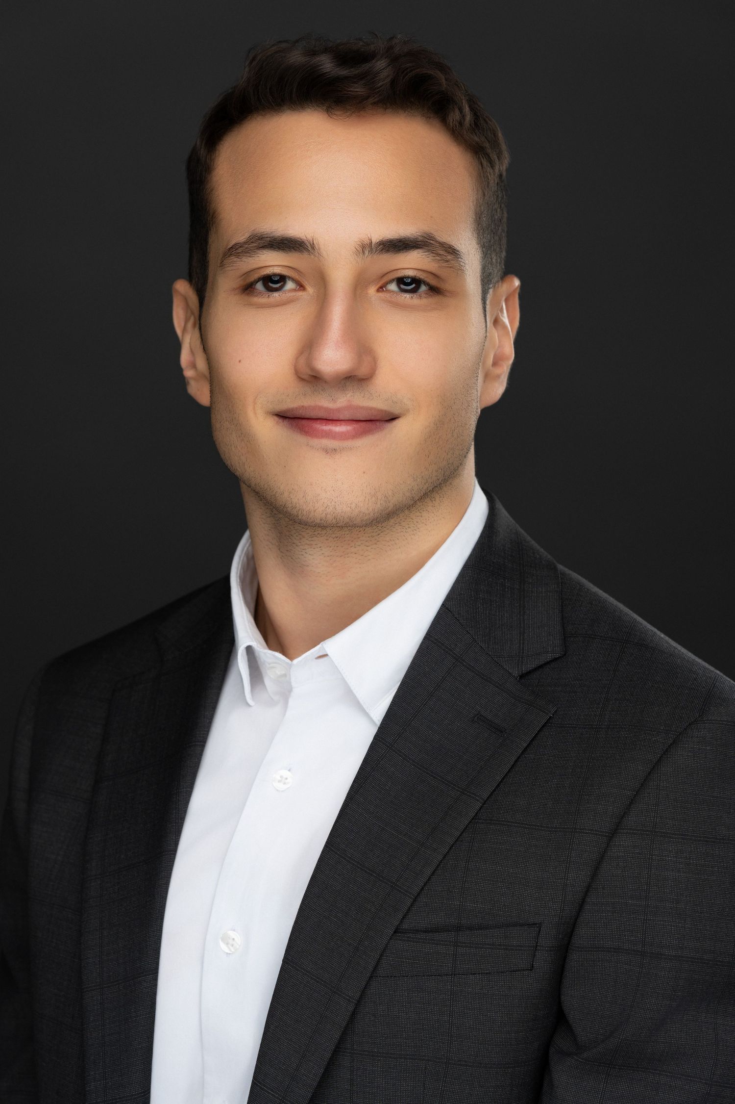 Professional male headshot with a clean, modern look, captured with soft studio lighting on a dark background.