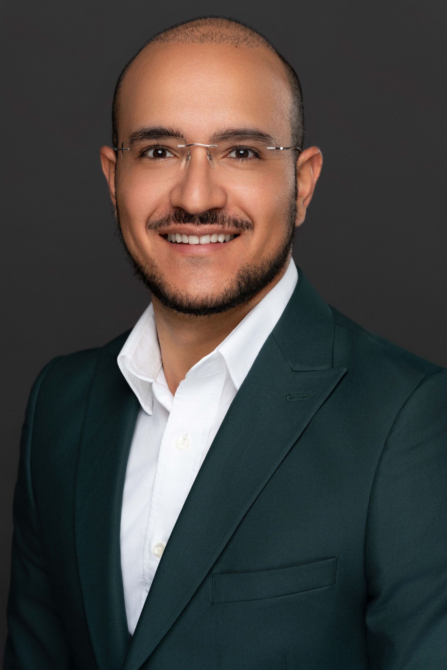 Corporate headshot of a smiling male professional in a green blazer with polished studio lighting.