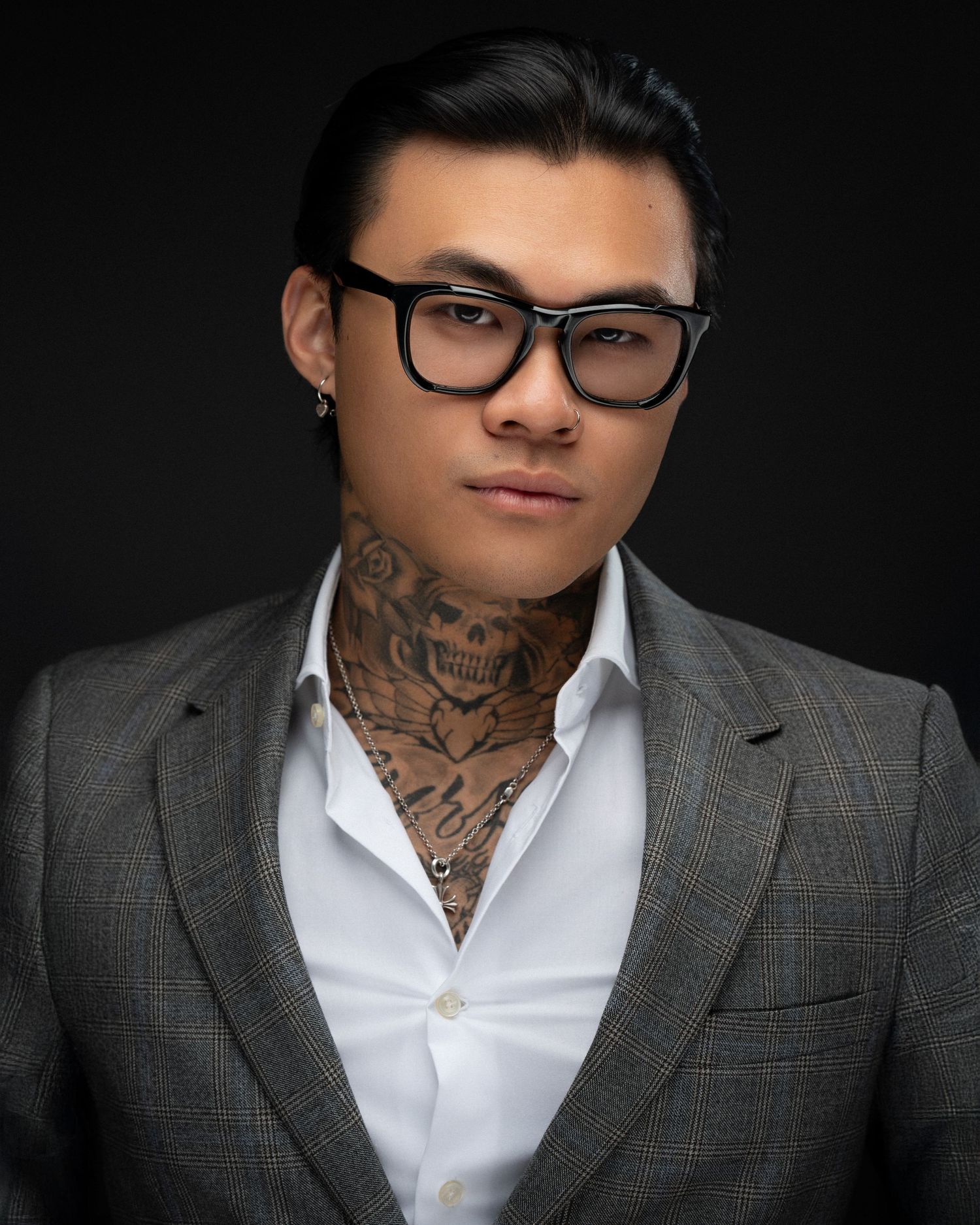 Editorial portrait of a male model with glasses and tattoos, styled in a suit with dramatic studio lighting.
