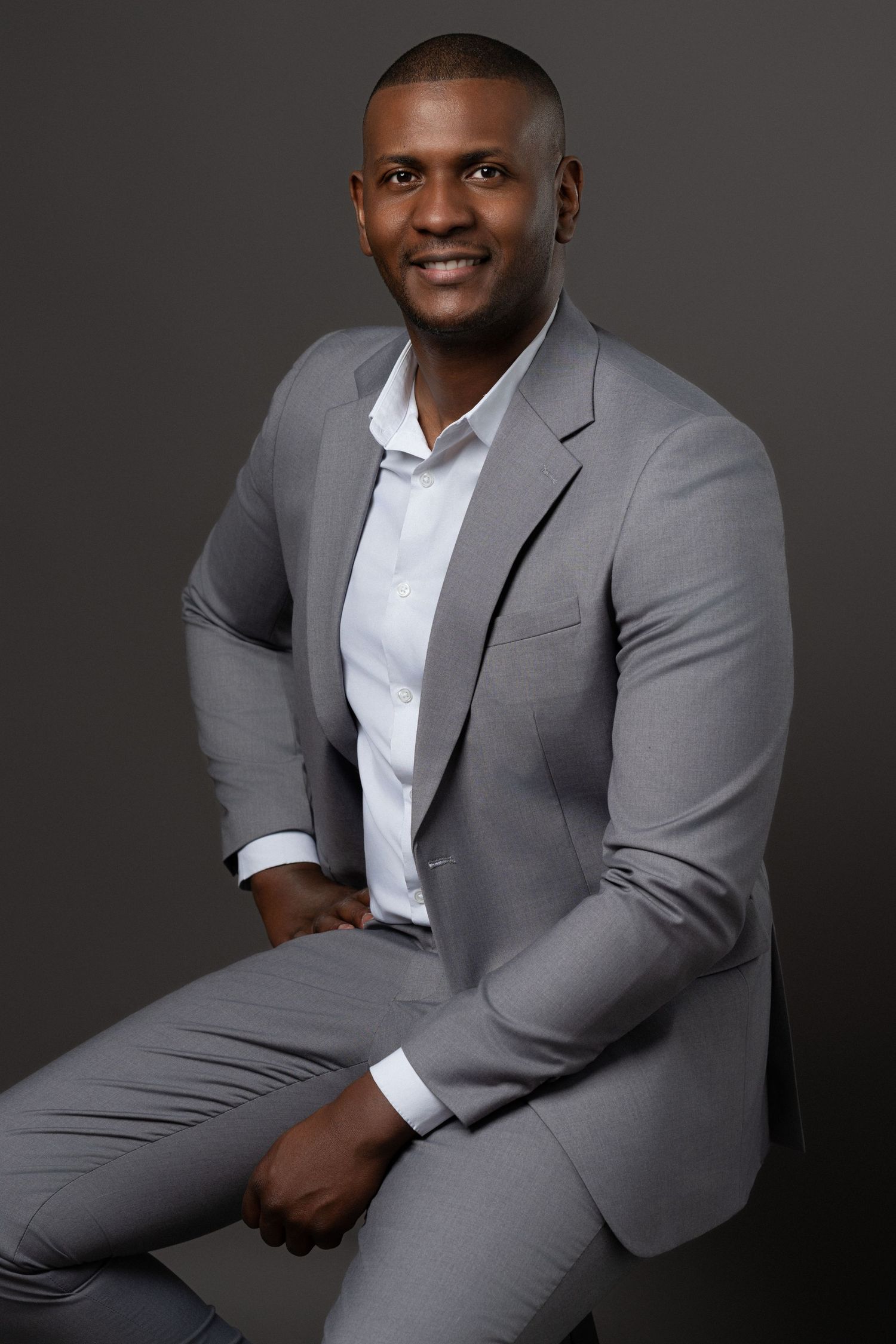Professional portrait of a male model in a light grey suit with a confident pose against a neutral studio background.