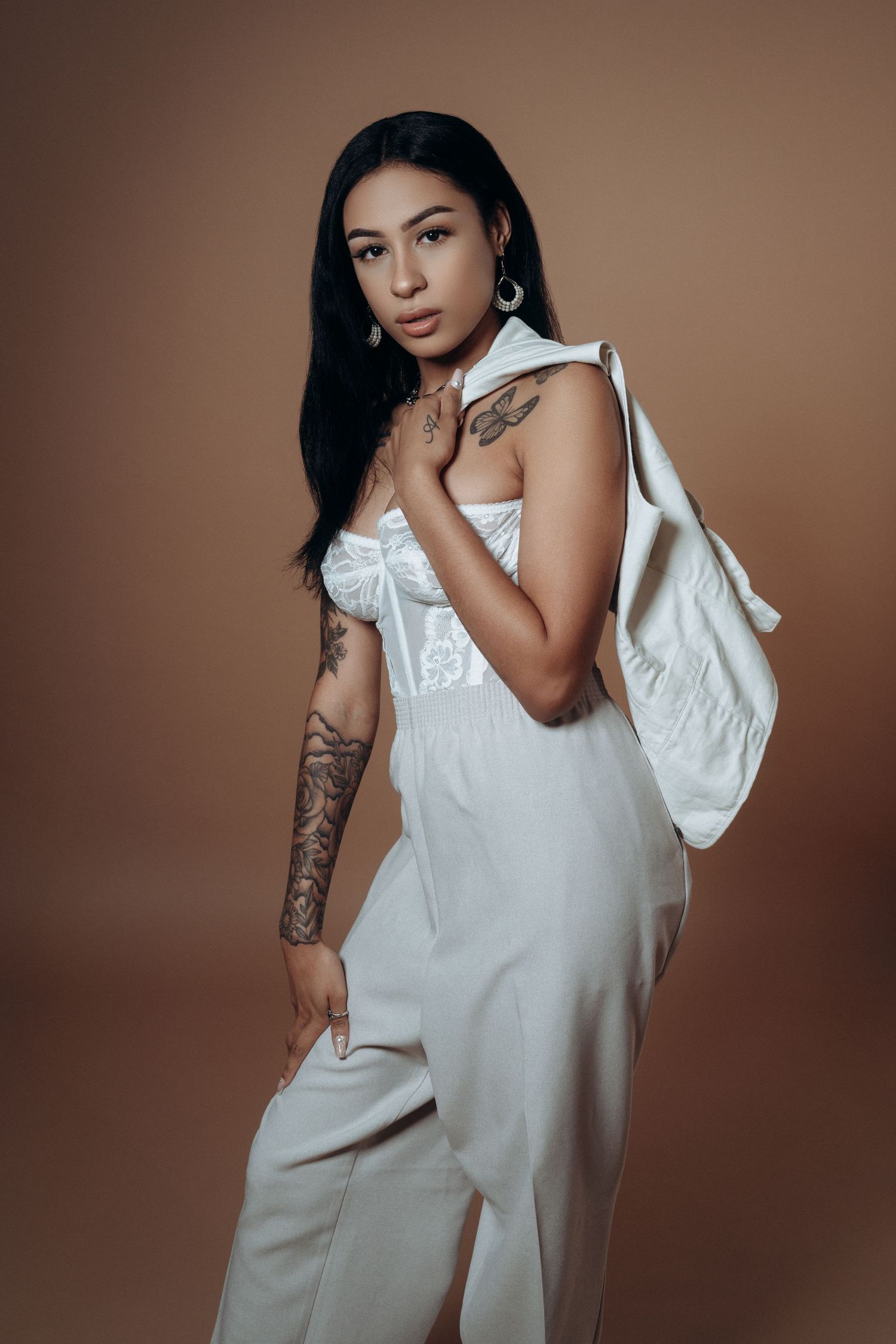 Editorial portrait of a female model in a white outfit against a warm mocha backdrop, photographed in a Montreal studio.