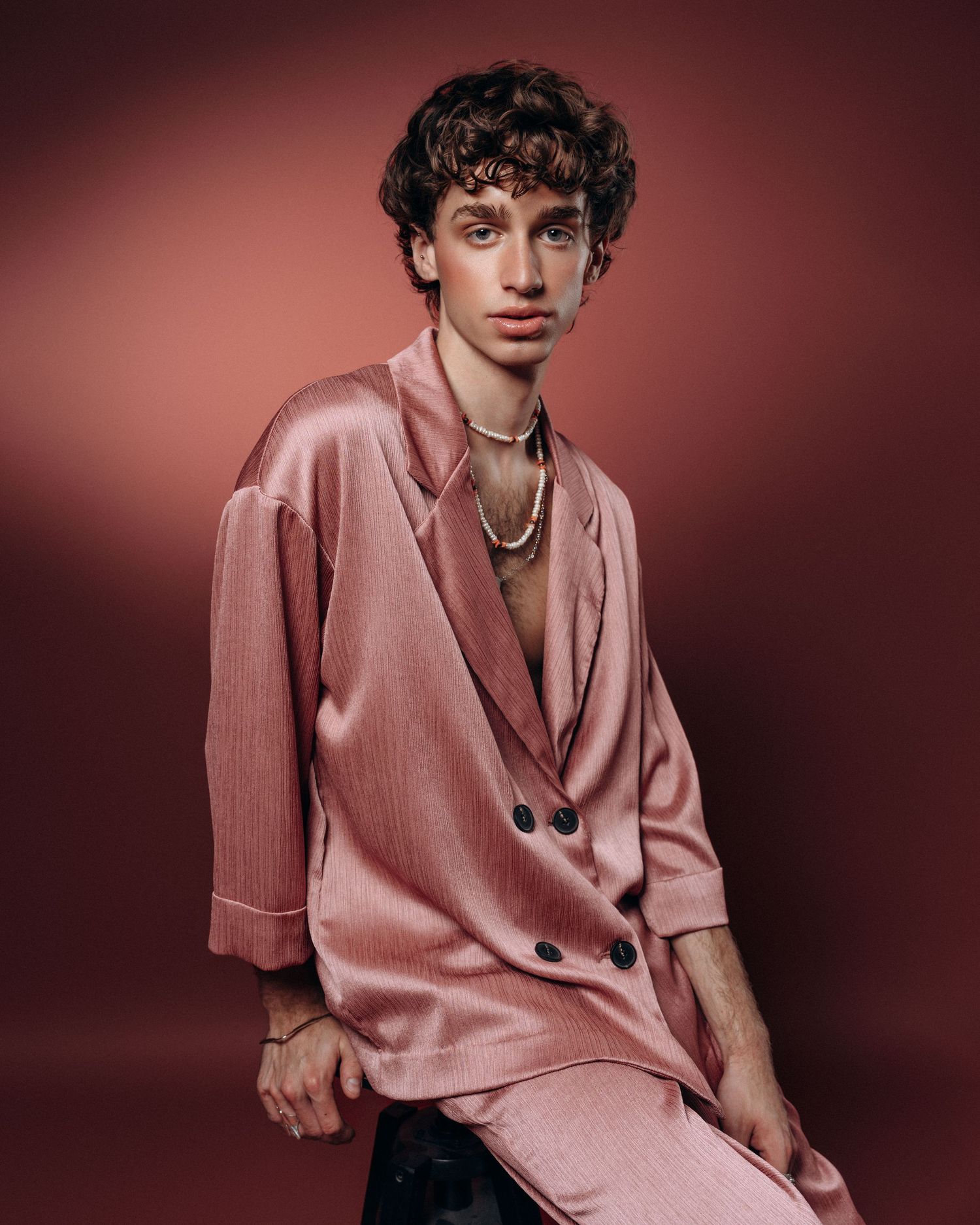 Editorial portrait of a man in a pink suit with statement jewelry on a pink background in a Montreal studio.