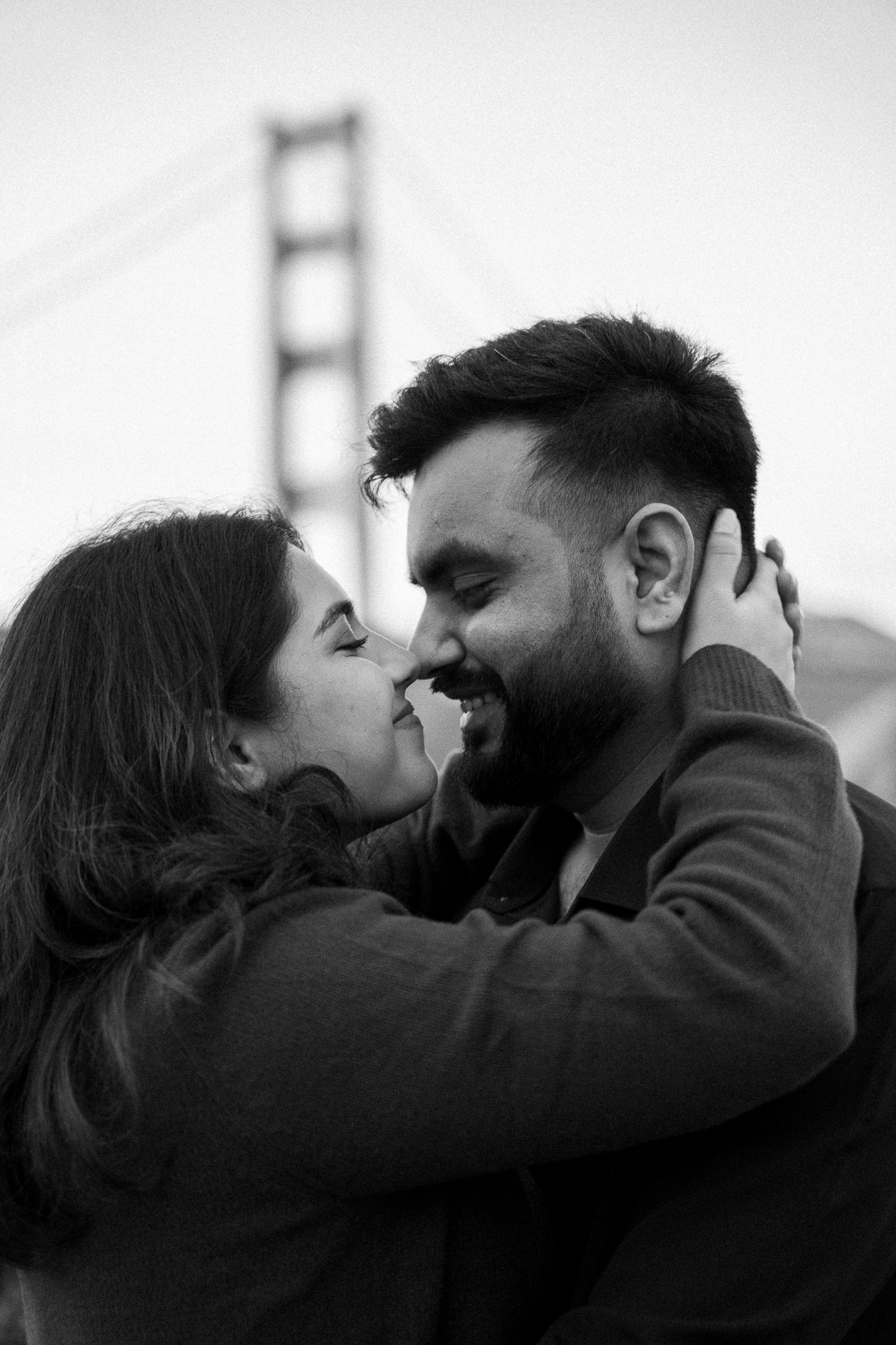 Monochrome image capturing the moment of an engagement proposal between two people, with the Golden Gate Bridge behind them