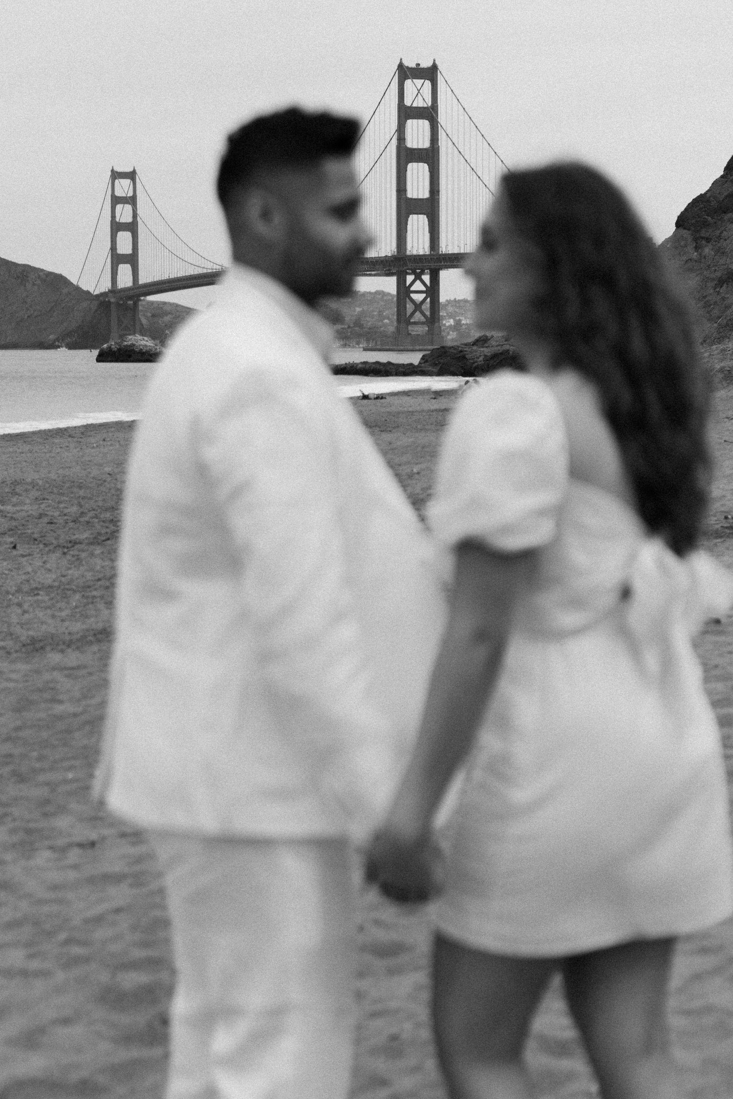 Monochrome image capturing the moment of an engagement proposal between two people, with the Golden Gate Bridge behind them