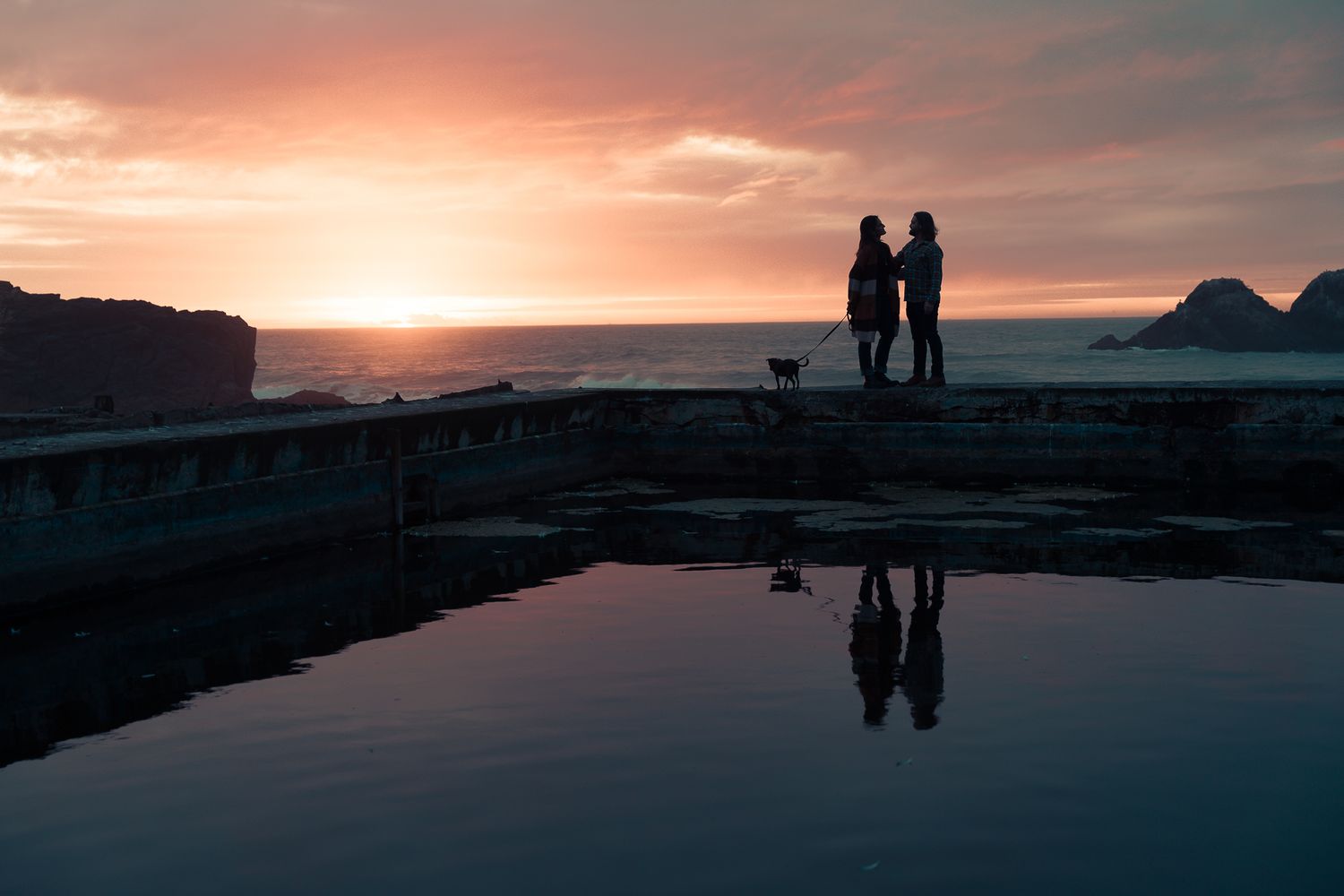image capturing the moment of an engagement proposal between two people, with the golden sunset Pacific Ocean stretching softly behind them