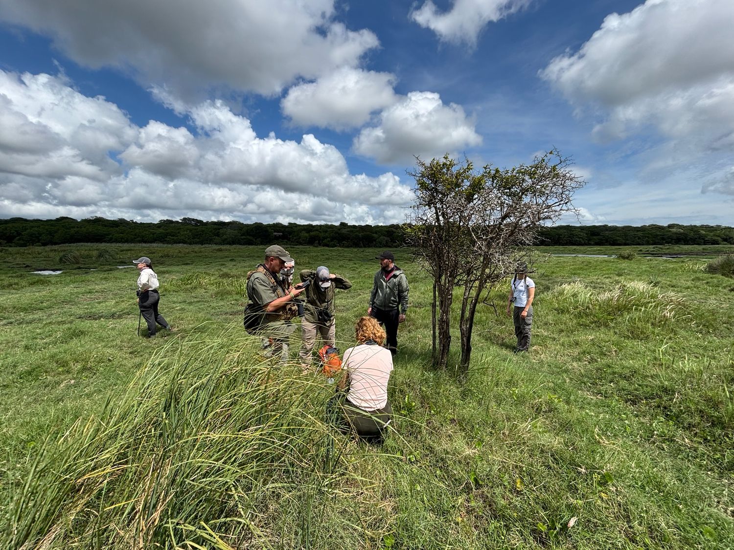 A group of people standing in a grassy field in South Africa with a cloudy sky in the background.