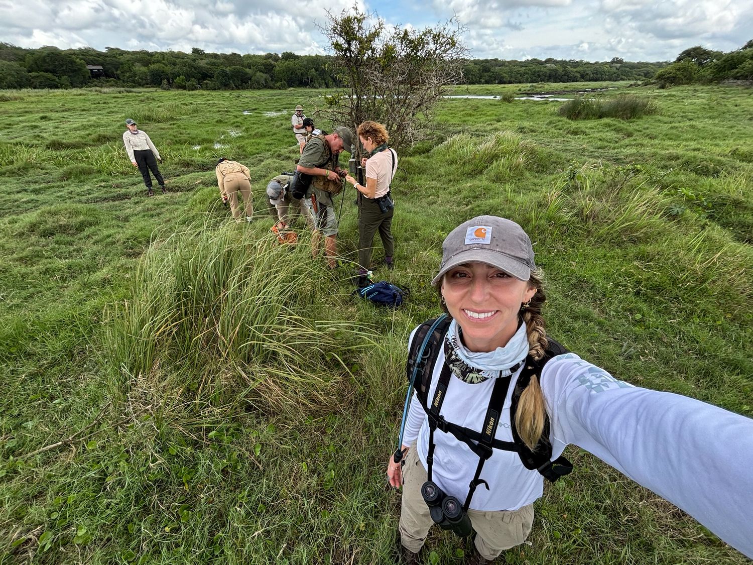 A person wearing a hat and backpack standing in a grassy field in South Africa with other people.