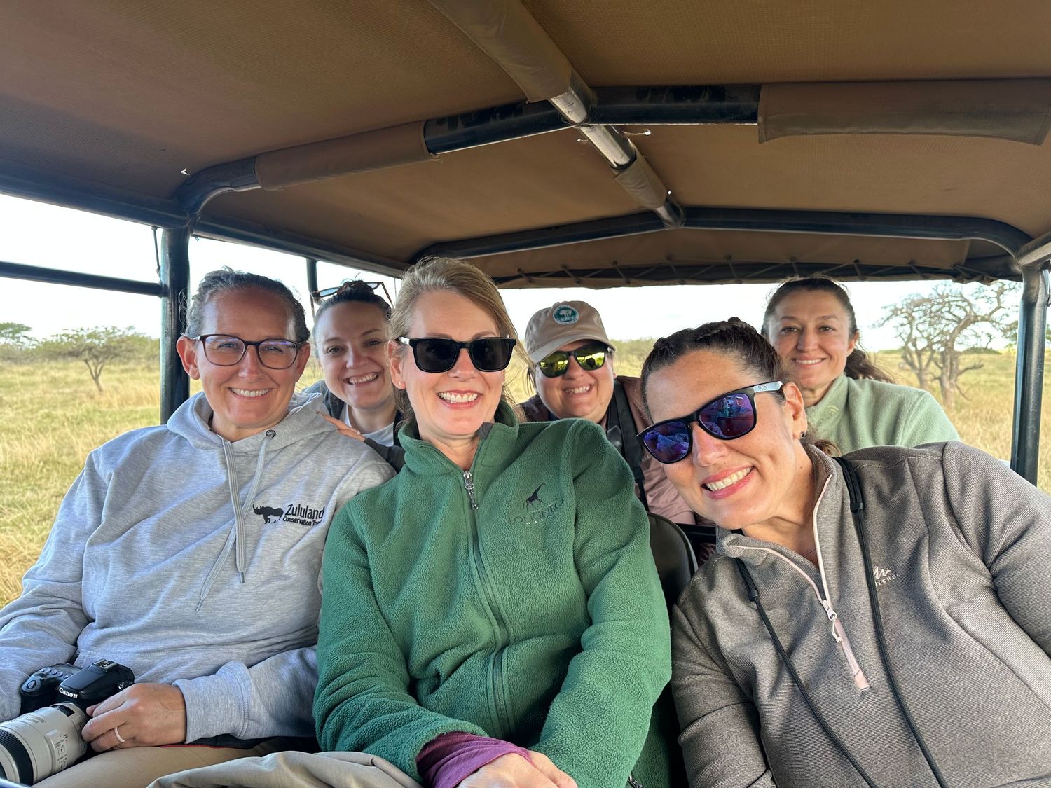 A group of people sitting together in a safari vehicle in an outdoor setting.