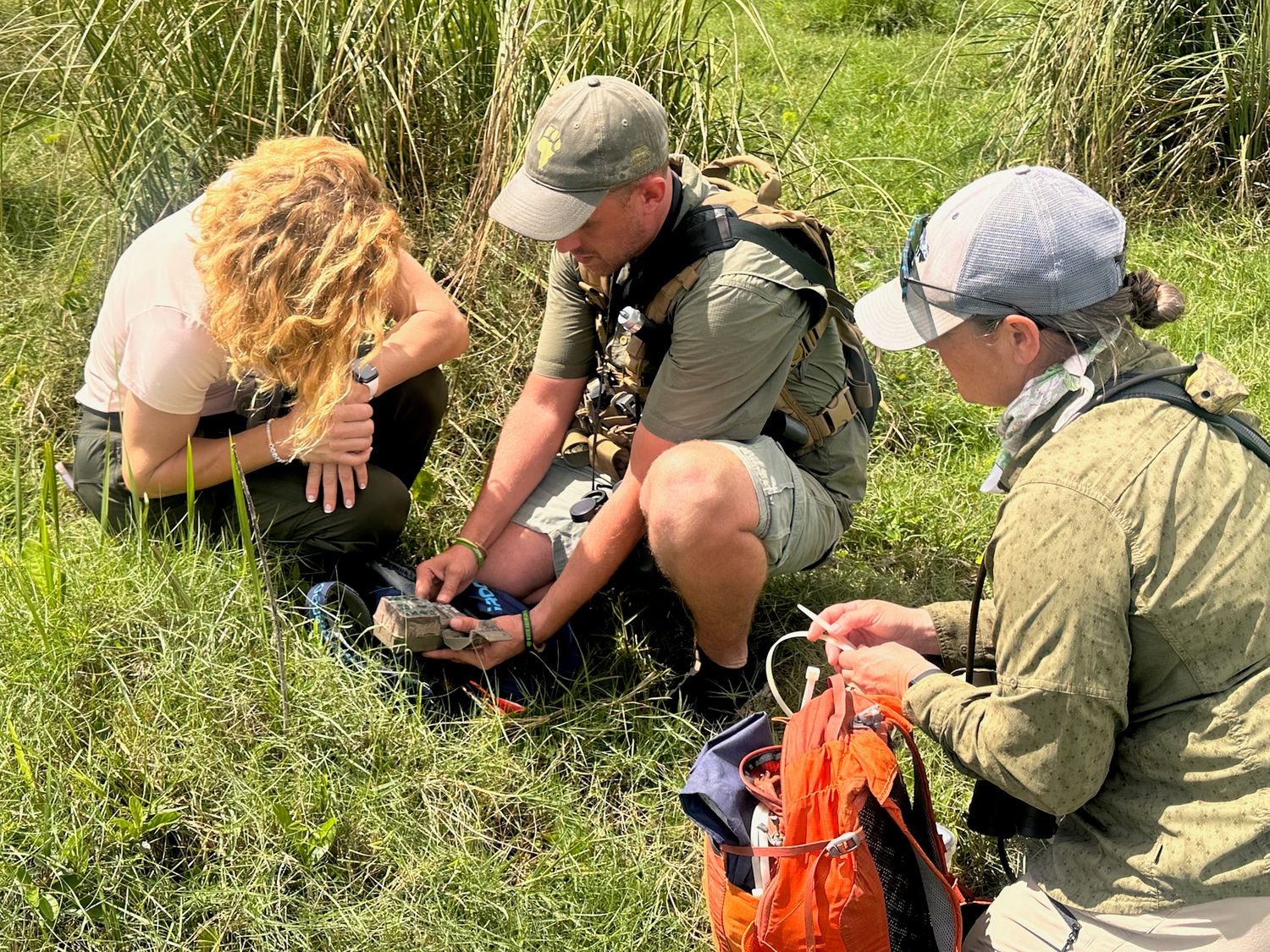 A group of people standing around a safari vehicle in a grassy, outdoor setting.